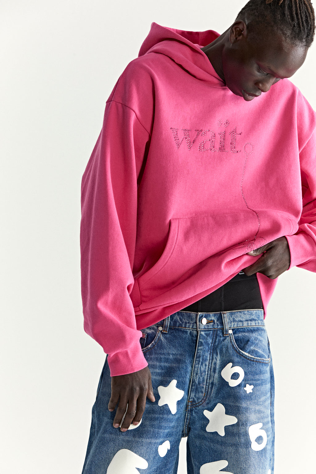 Pink WAIT STONE HOODIE with rhinestone "Wait" detail, kangaroo pocket, and rib knit trim, paired with star-print jeans.