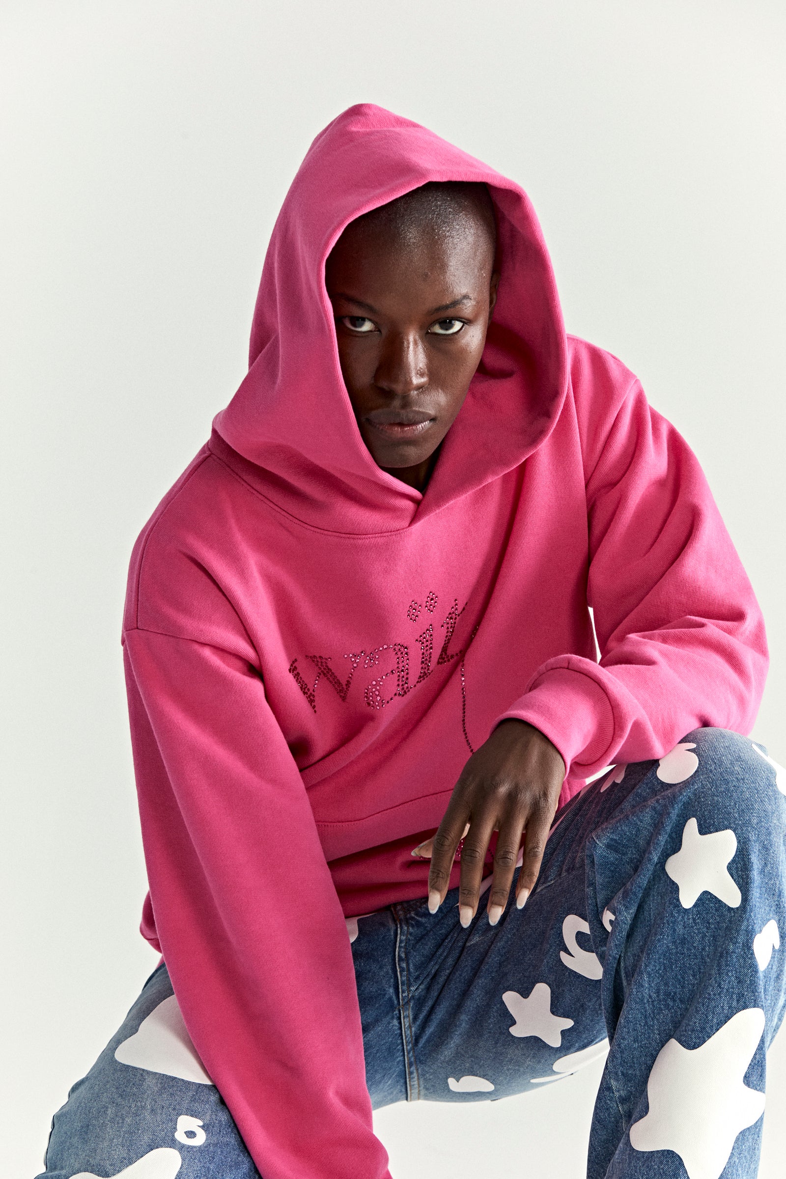 Model wearing a pink WAIT STONE HOODIE with rhinestone "Wait" detail, kangaroo pocket, and rib knit cuffs.