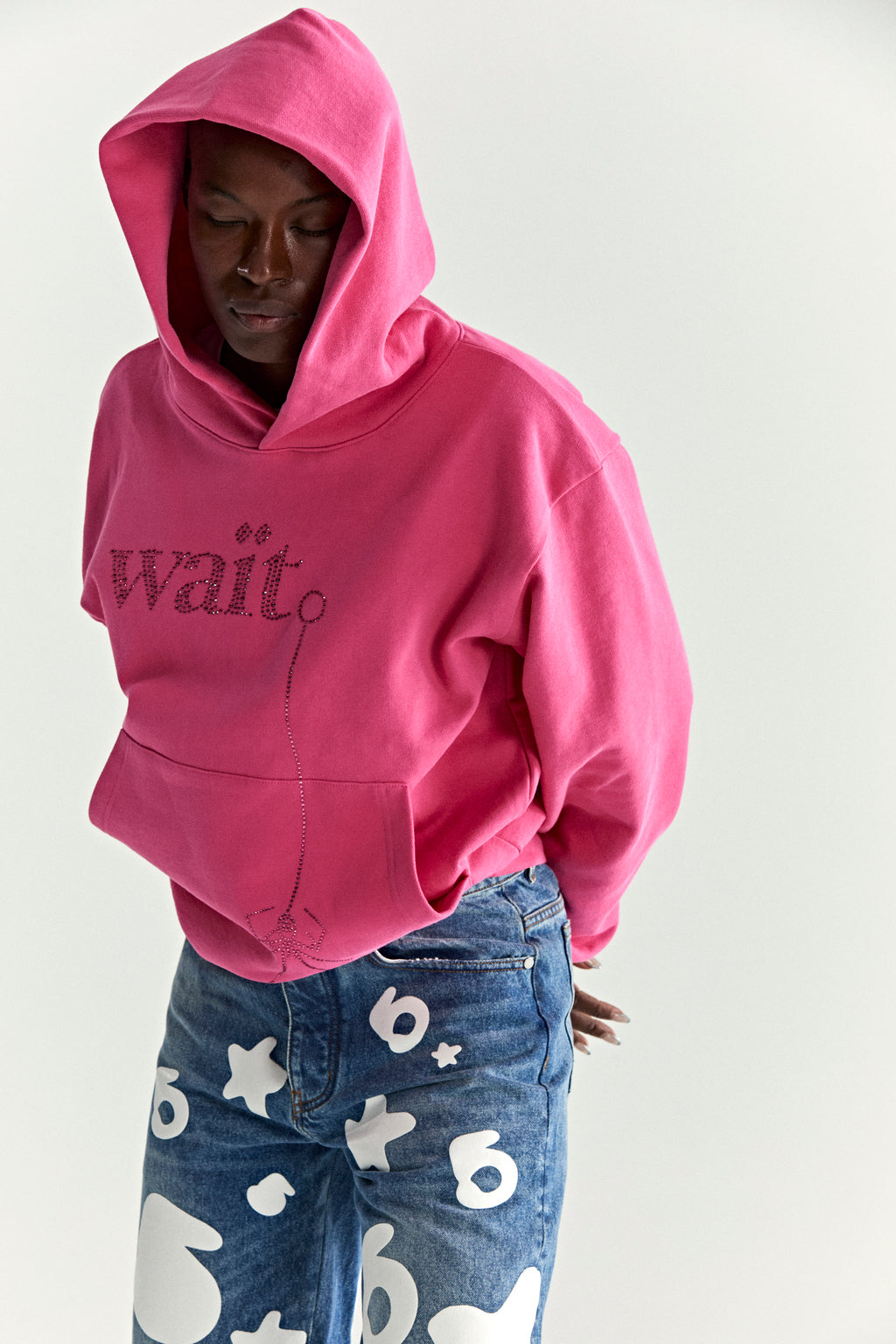 Pink WAIT STONE HOODIE with rhinestone "Wait" detail, kangaroo pocket, and rib knit trim.