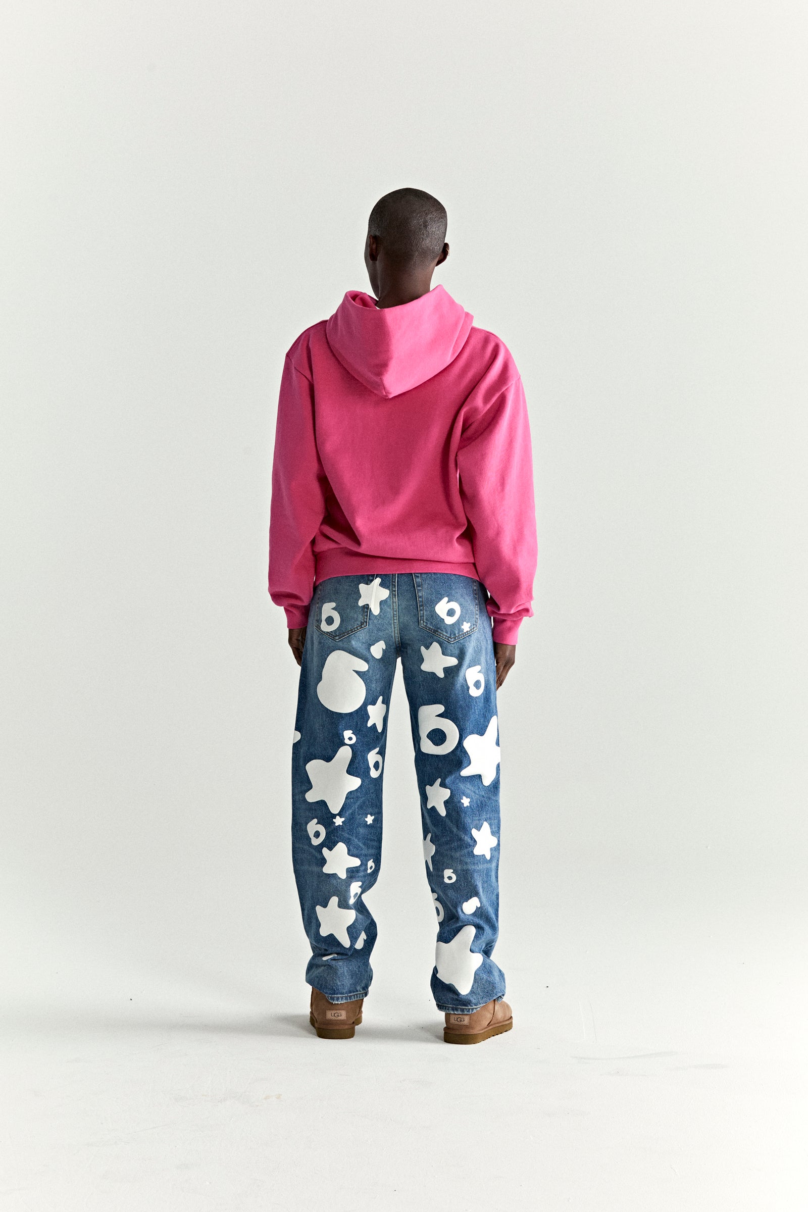 Back view of a person wearing a pink WAIT STONE HOODIE and blue jeans with white star and number 6 graphics.