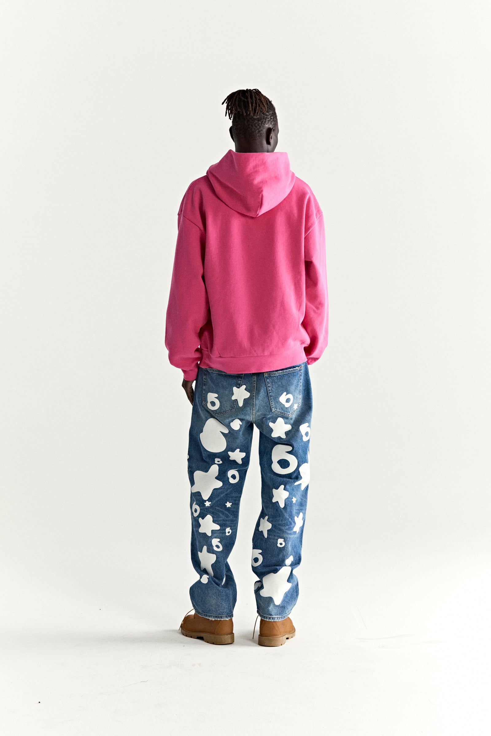 Back of a person wearing an oversized pink fleece hoodie and blue jeans with white star and number designs.