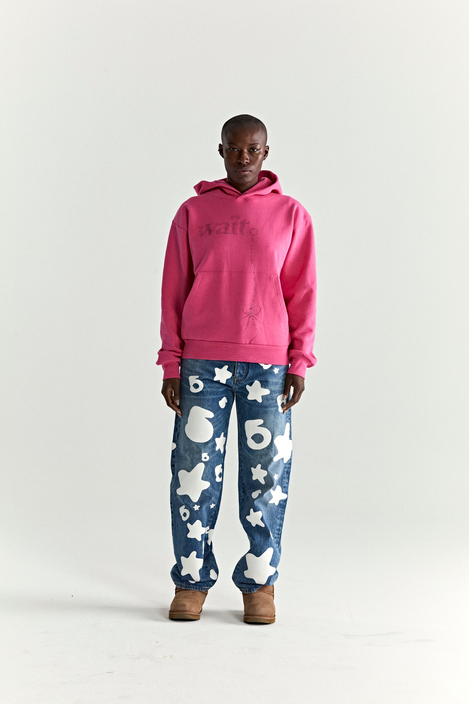 Model wearing a pink WAIT STONE HOODIE with rhinestone "Wait" detail, kangaroo pocket, and rib knit trim.
