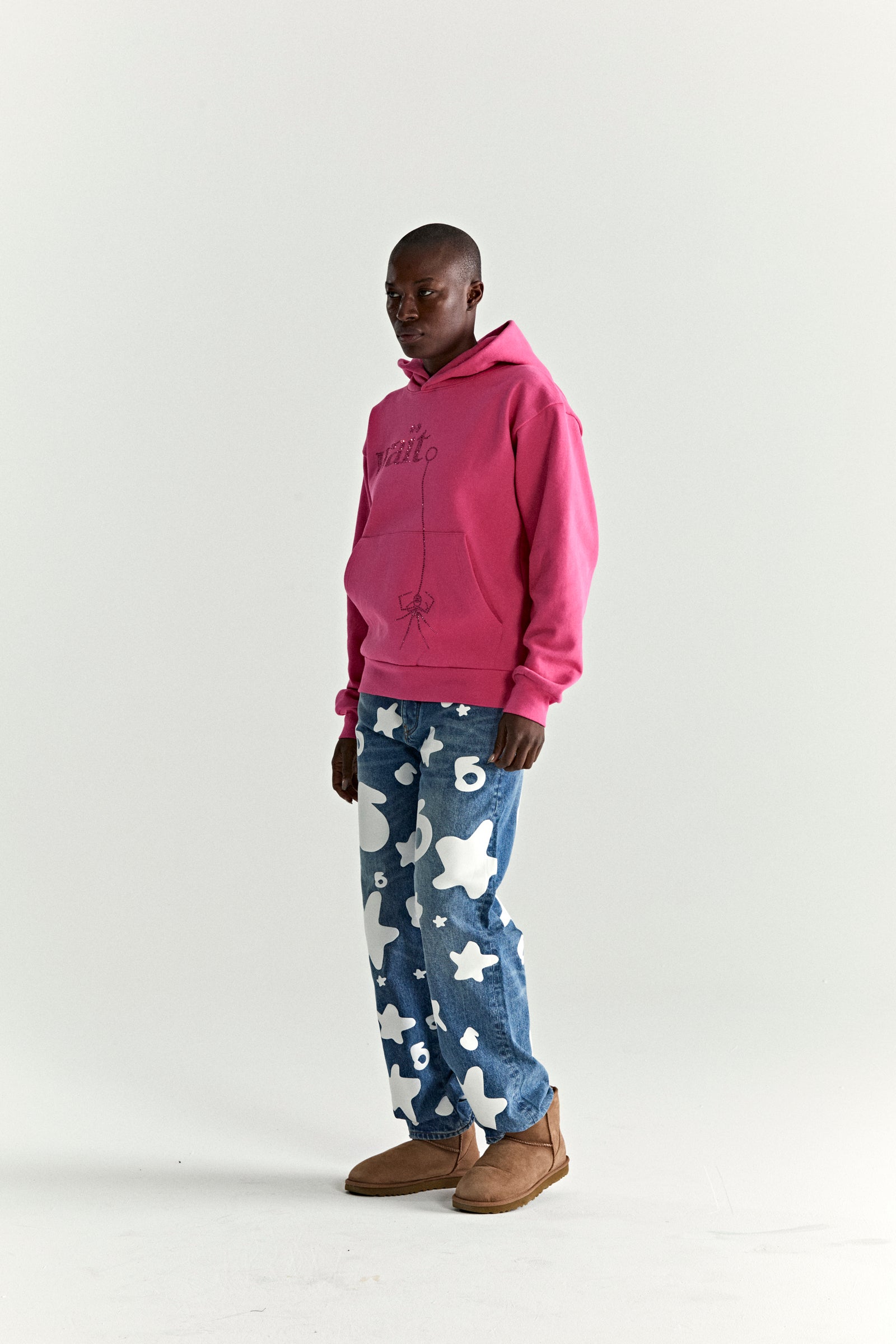 Model wearing a pink WAIT STONE HOODIE with rhinestone detail, kangaroo pocket, and rib knit trim.
