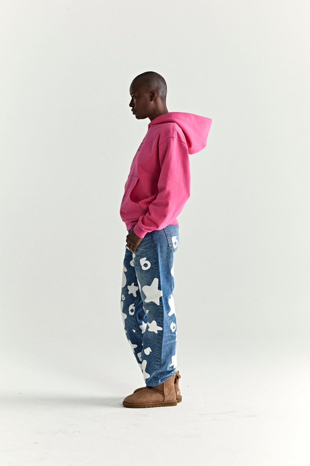 Model in pink WAIT STONE HOODIE, blue jeans with white stars, and brown boots.