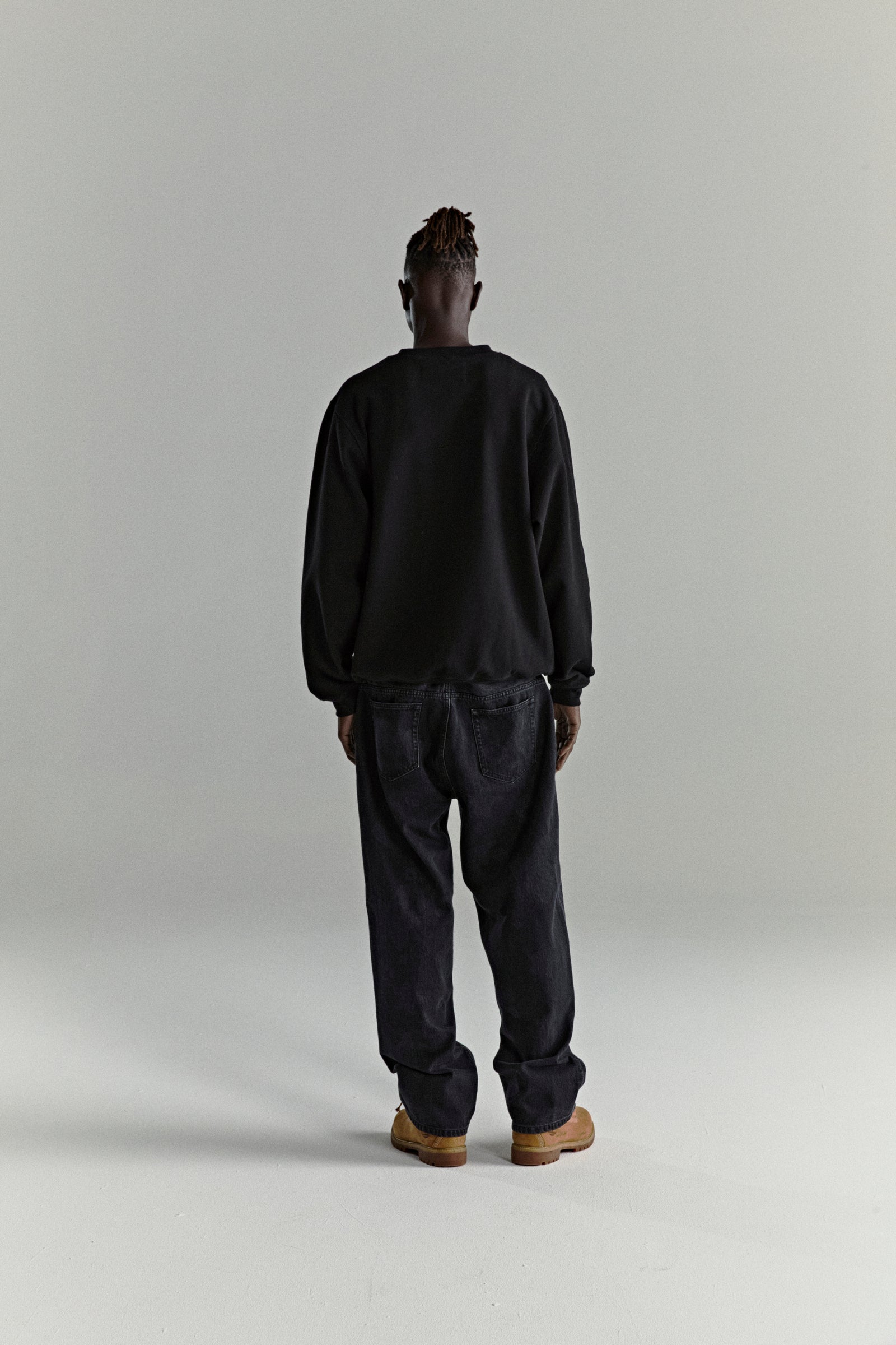 Man in black CORE CREWNECK, 13oz brushed fleece, and dark jeans, viewed from behind.