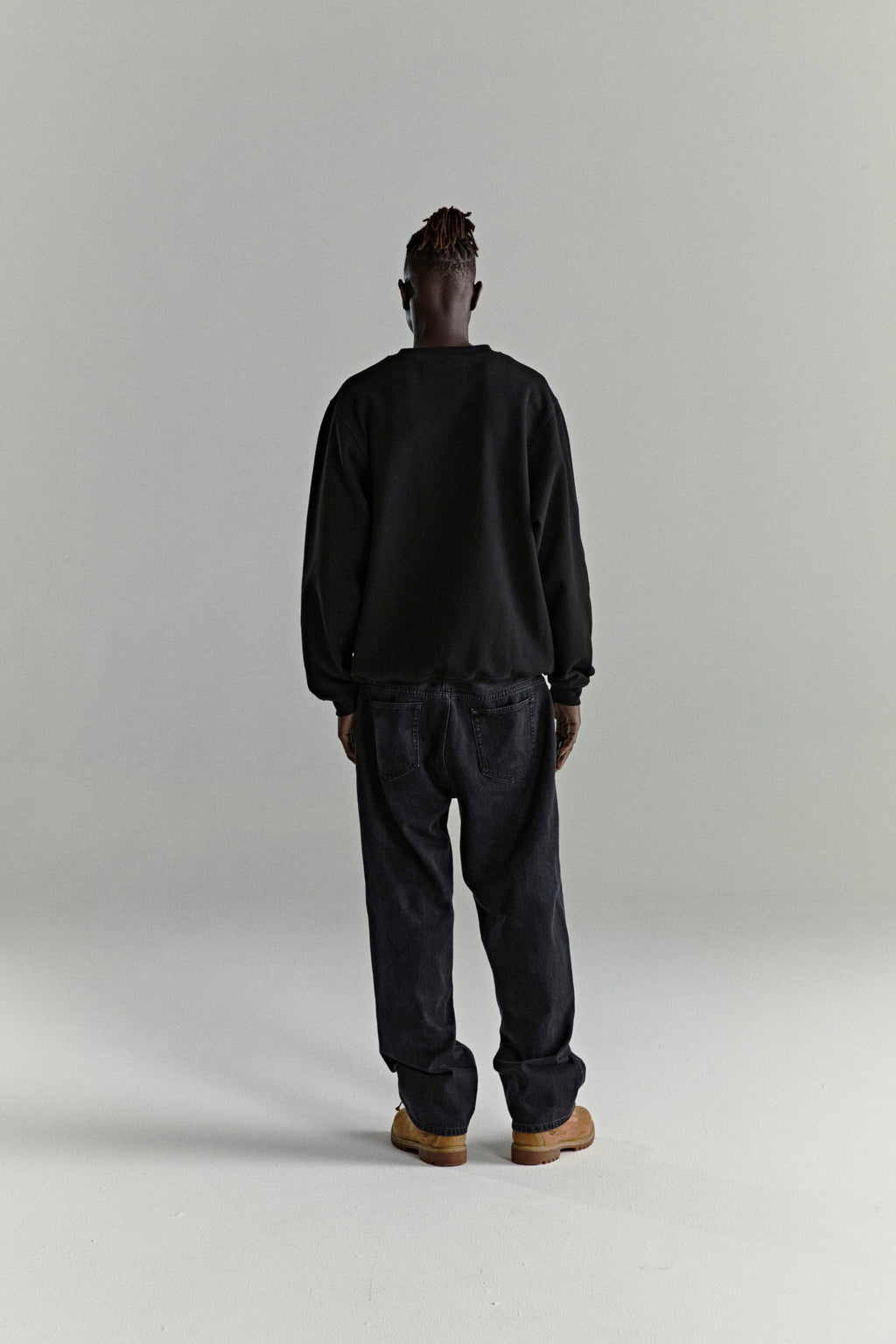 Man in black CORE CREWNECK, 13oz brushed fleece, and dark jeans, viewed from behind.
