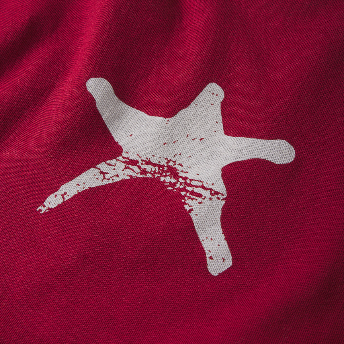 Red 100% cotton long sleeve tee featuring a distressed white star graphic print on the fabric.