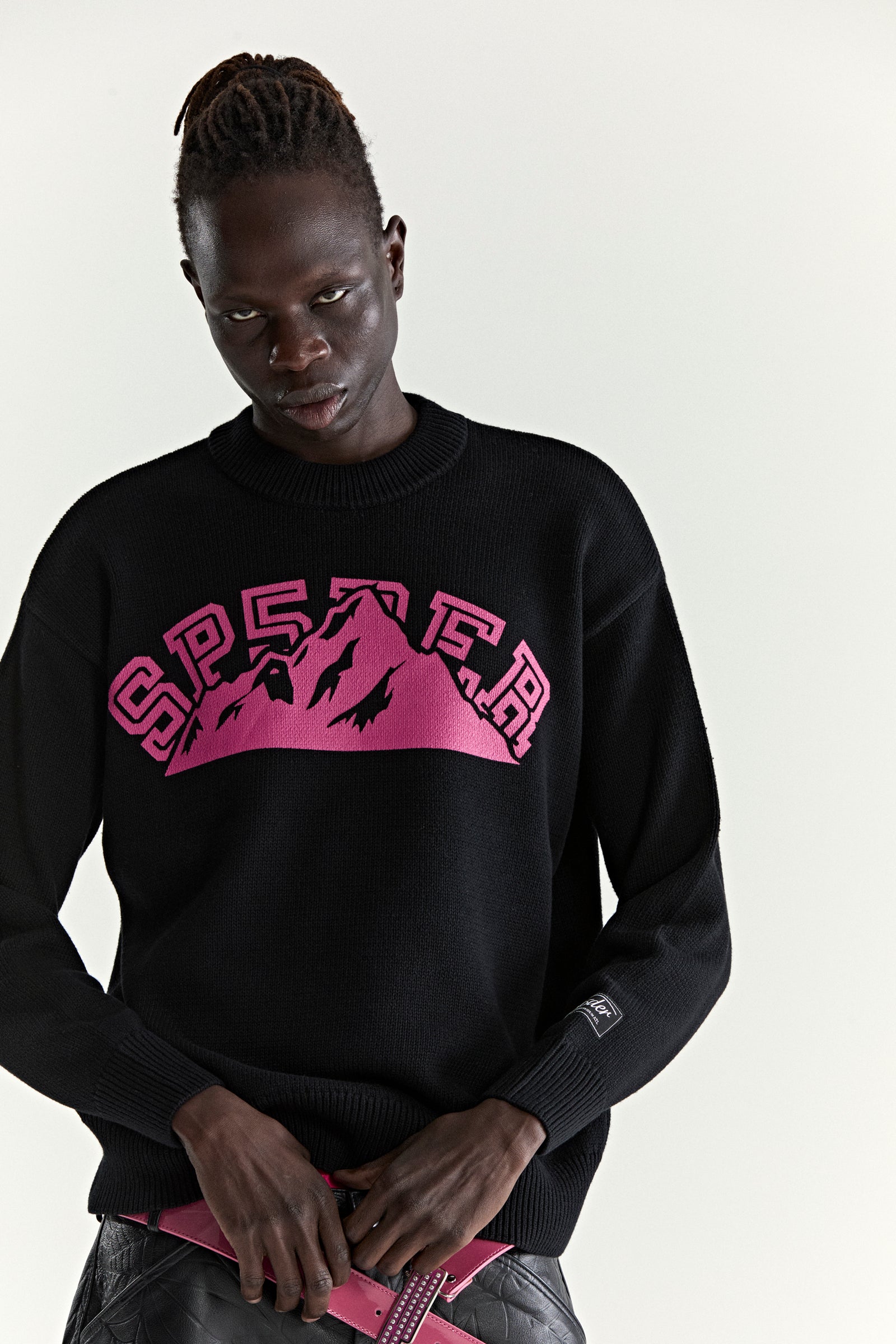 Black knitted sweater with pink "SP5DER" mountain graphic, ribbed trim, and sleeve patch.