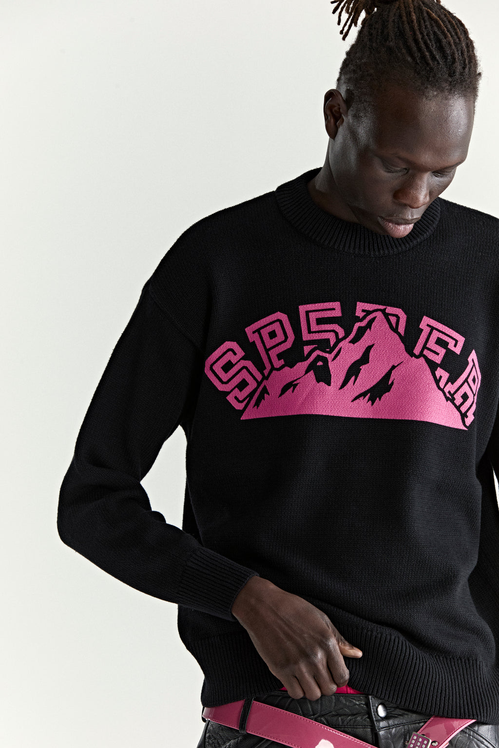 Black knitted sweater with pink "SP5DER" mountain graphic, ribbed collar, cuffs, and hem.