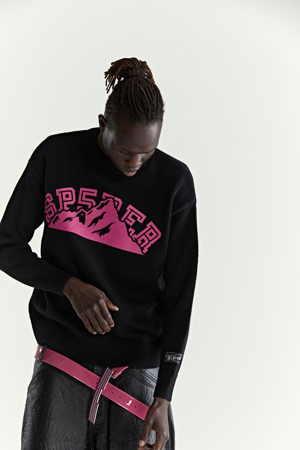 Black knitted sweater with pink "SP5DER" mountain graphic, ribbed trim, and sleeve patch.