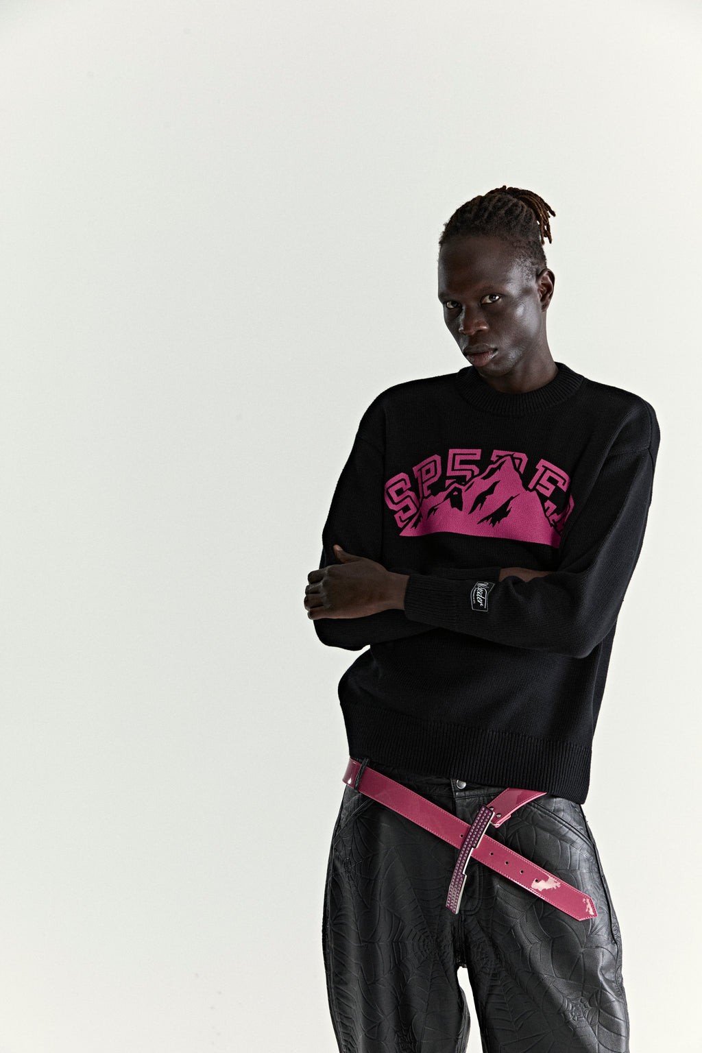 Black knitted sweater with pink "SP5DER" mountain graphic, ribbed trims, and sleeve patch.