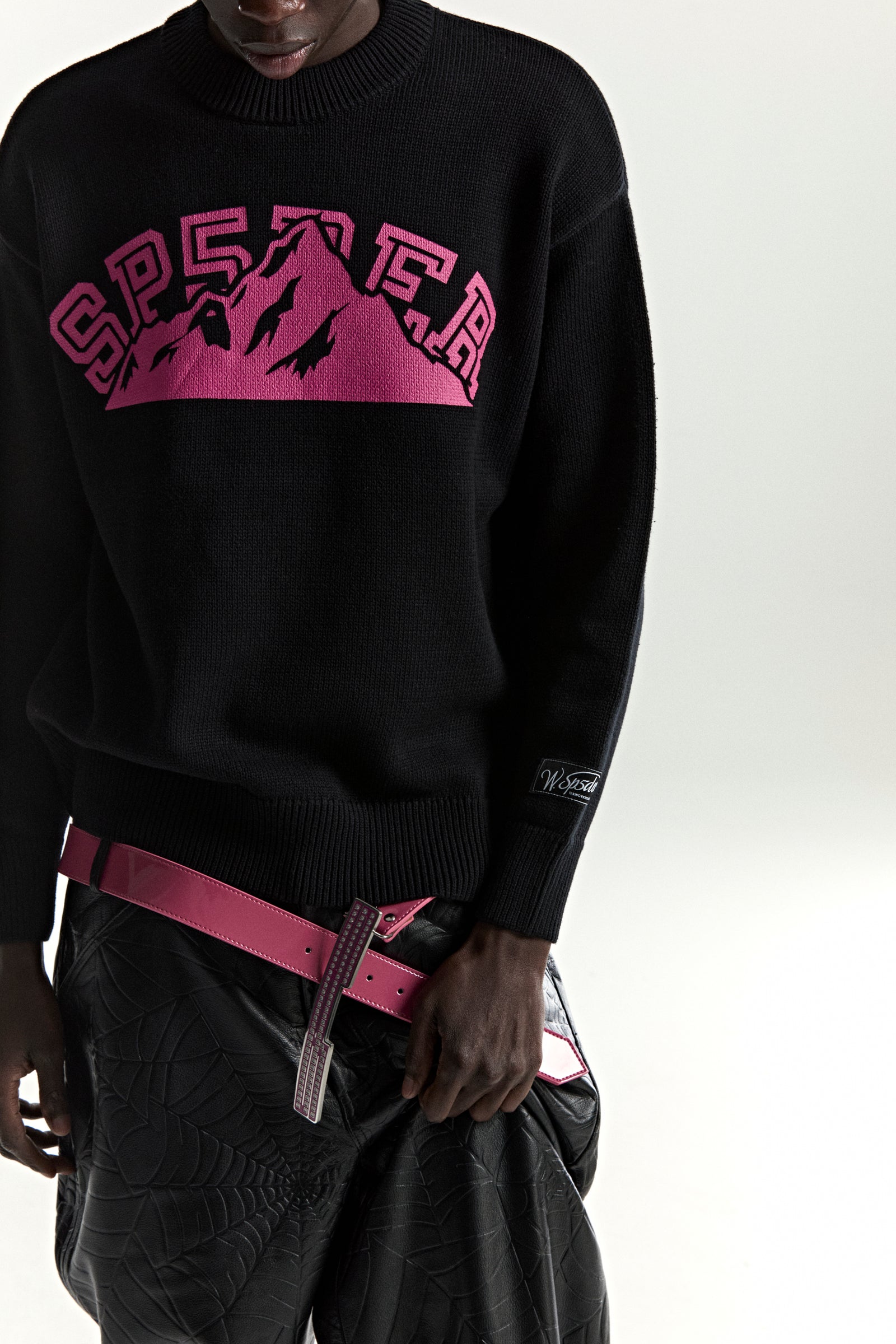 Black knitted MOUNTAIN VALLEY SWEATER with a pink SP5DER mountain graphic and sleeve patch.