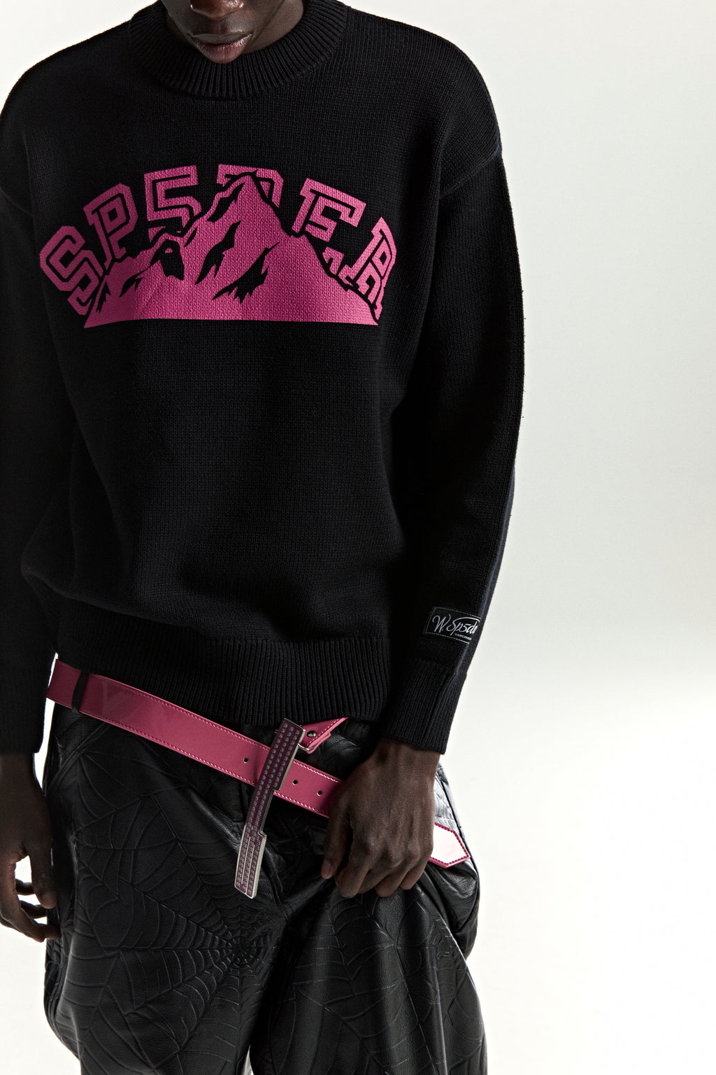 Black knitted MOUNTAIN VALLEY SWEATER with a pink SP5DER mountain graphic and sleeve patch.