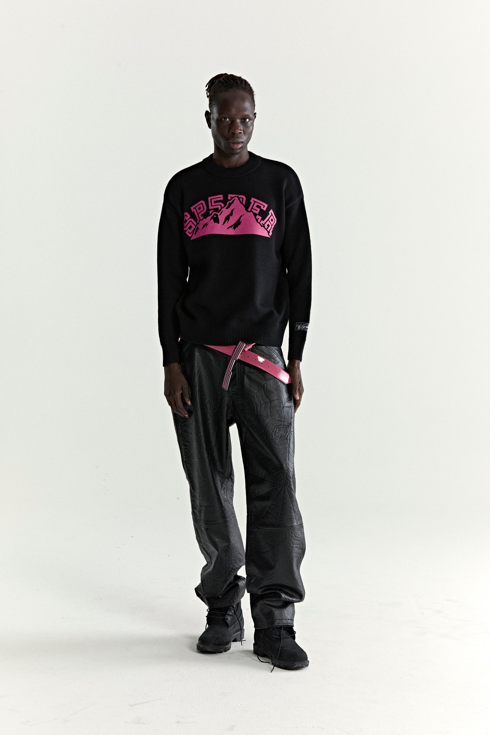 Black knitted sweater with pink "SP5DER" mountain graphic, ribbed trim, and sleeve patch.