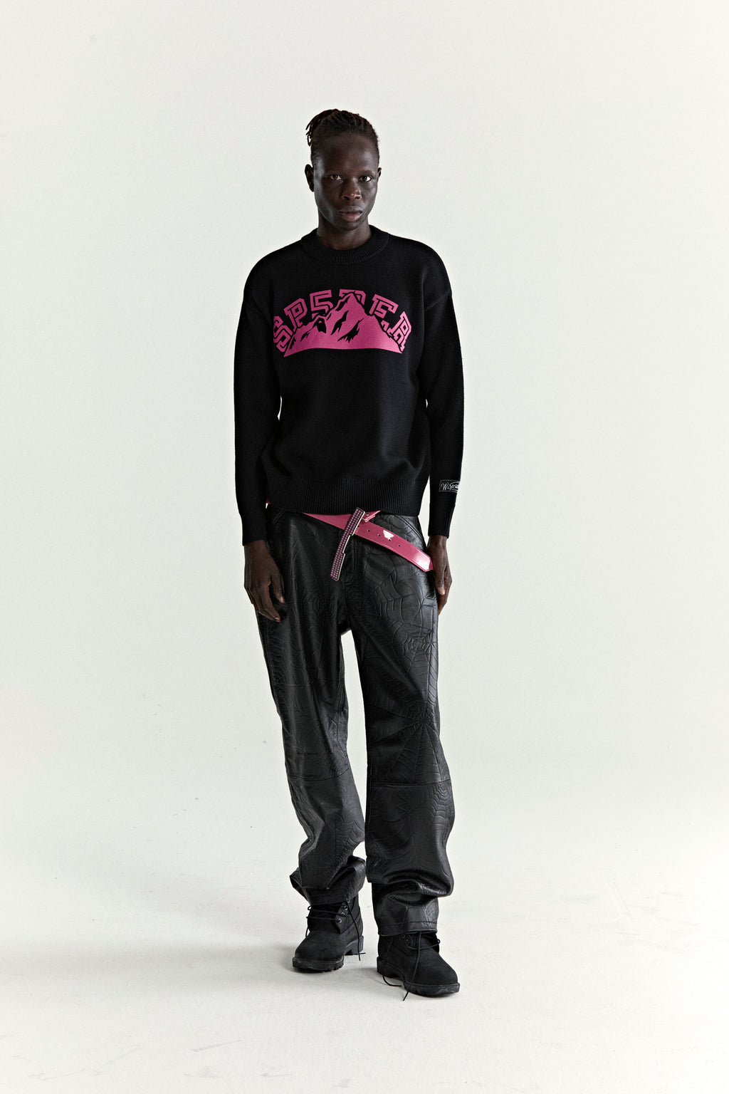 Black knitted sweater with pink "SP5DER" mountain graphic, ribbed trim, and sleeve patch.