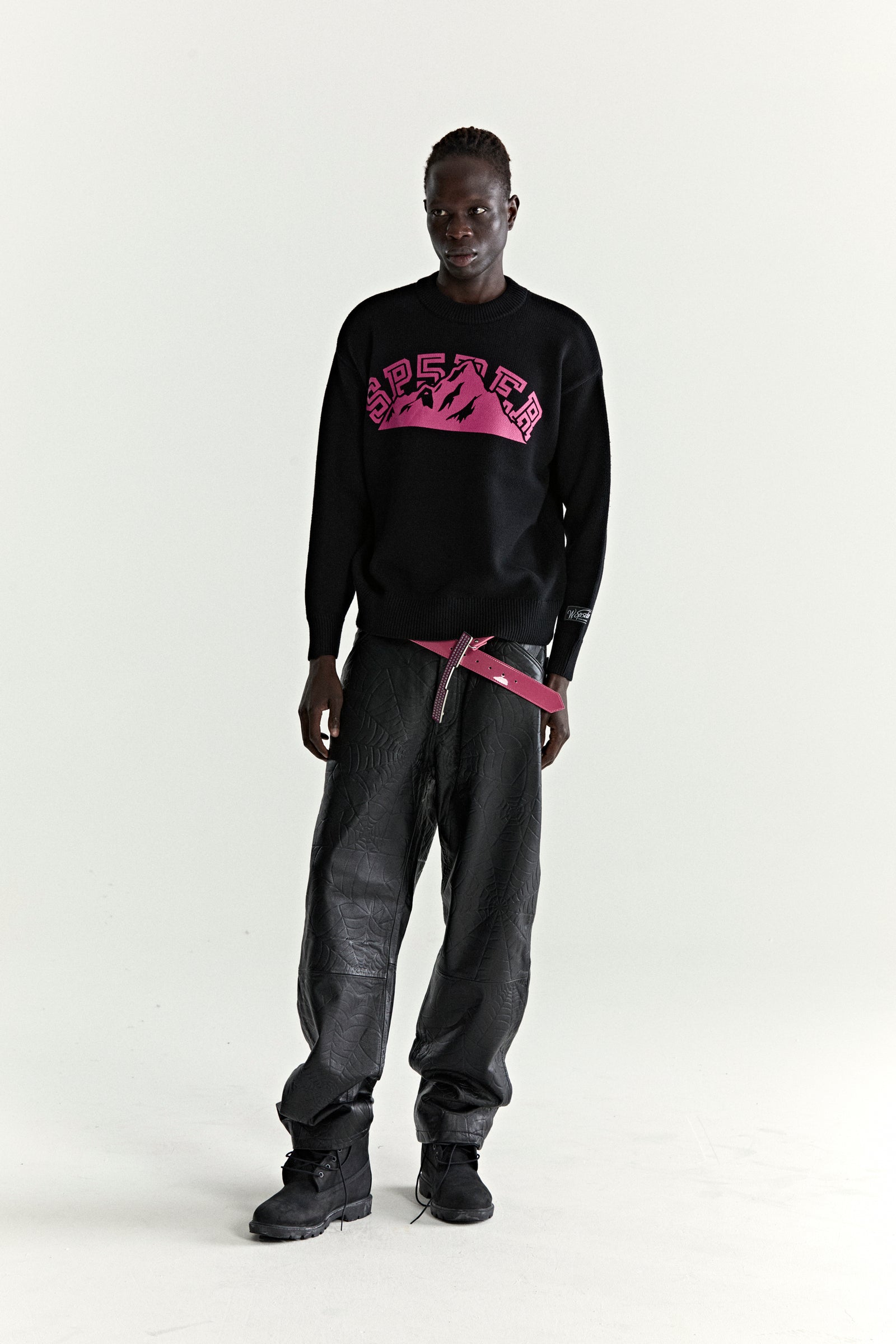 Black knitted MOUNTAIN VALLEY SWEATER with pink SP5DER graphic, ribbed trim, and sleeve patch.