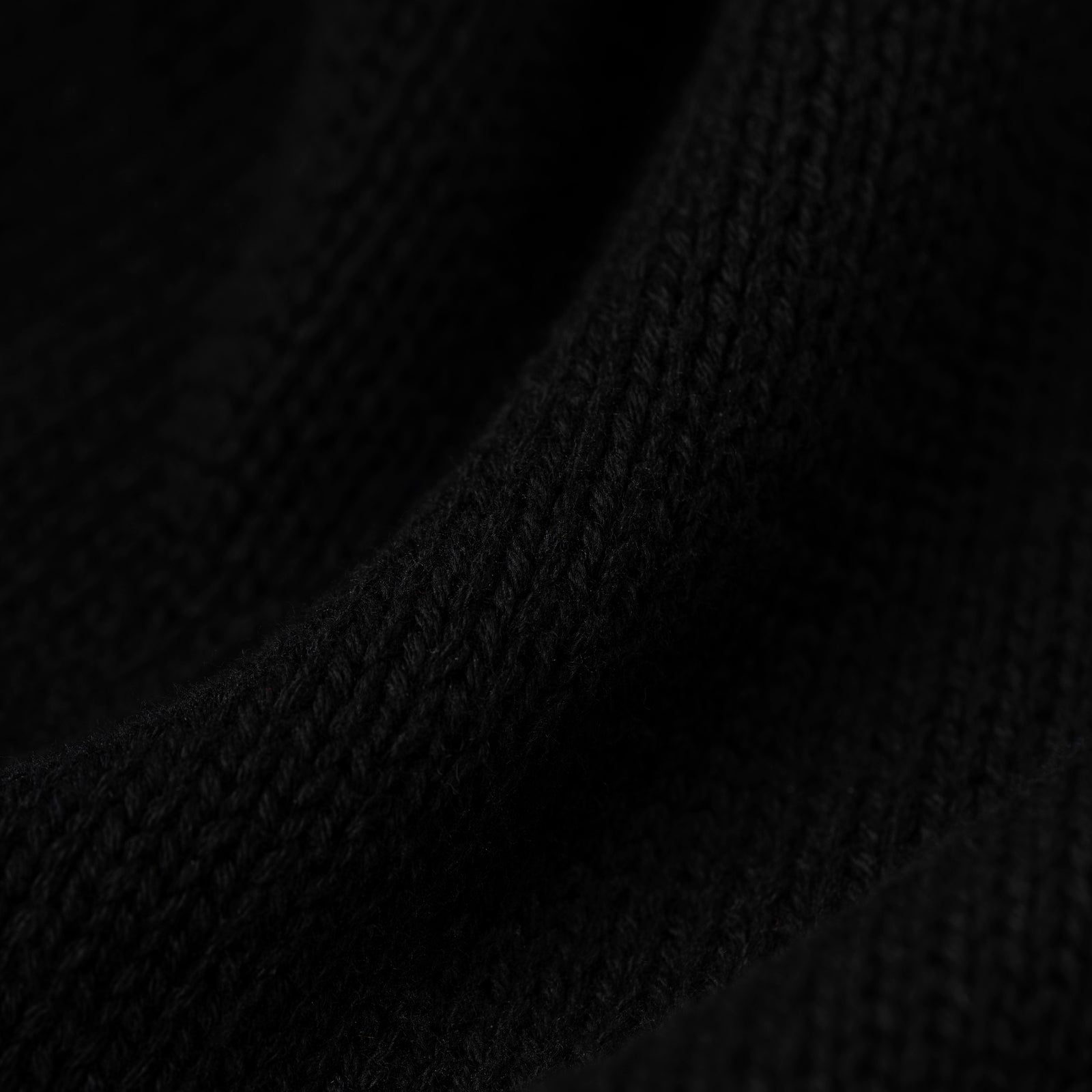 Close-up of a black knitted sweater fabric with visible texture and subtle folds.