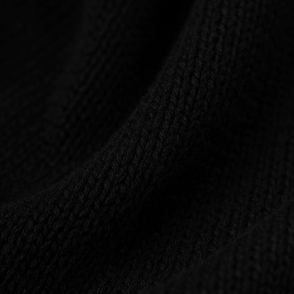 Close-up of a black knitted sweater fabric with visible texture and subtle folds.