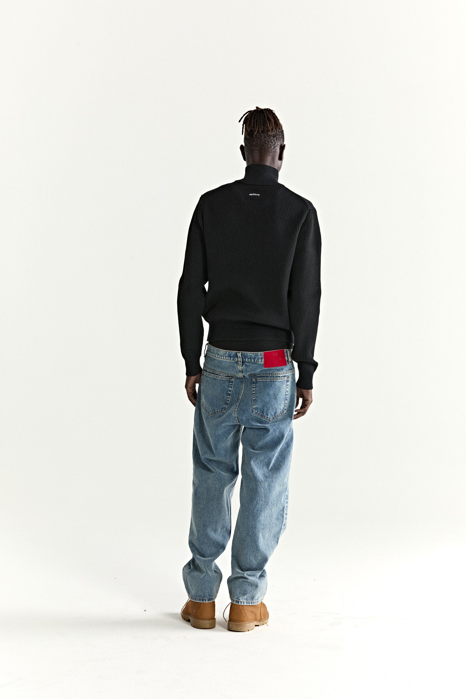 Black rib knit wool/cotton blend zip sweater with graphic at chest, worn with blue jeans.