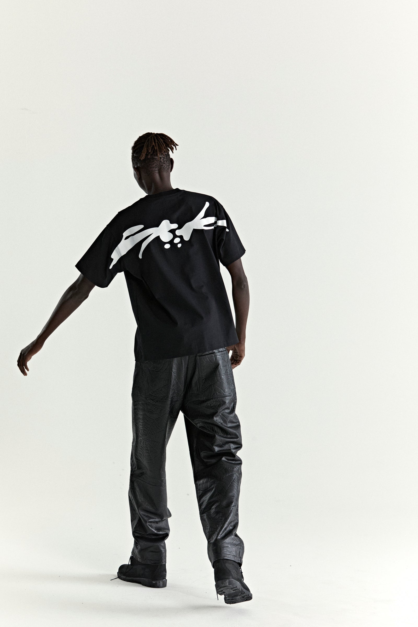 Black 100% cotton TM TEE with white graphic print on back, worn by a person in black pants.