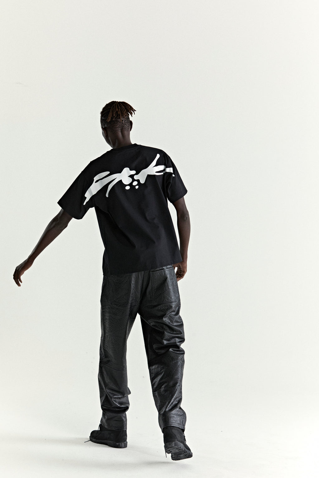 Black 100% cotton TM TEE with white graphic print on back, worn by a person in black pants.