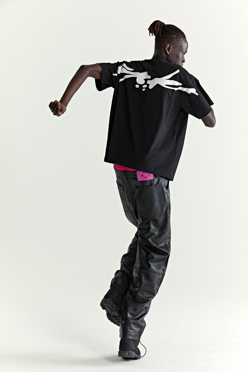 Black 100% cotton TM TEE with white graphic print on back, worn by a person in motion.