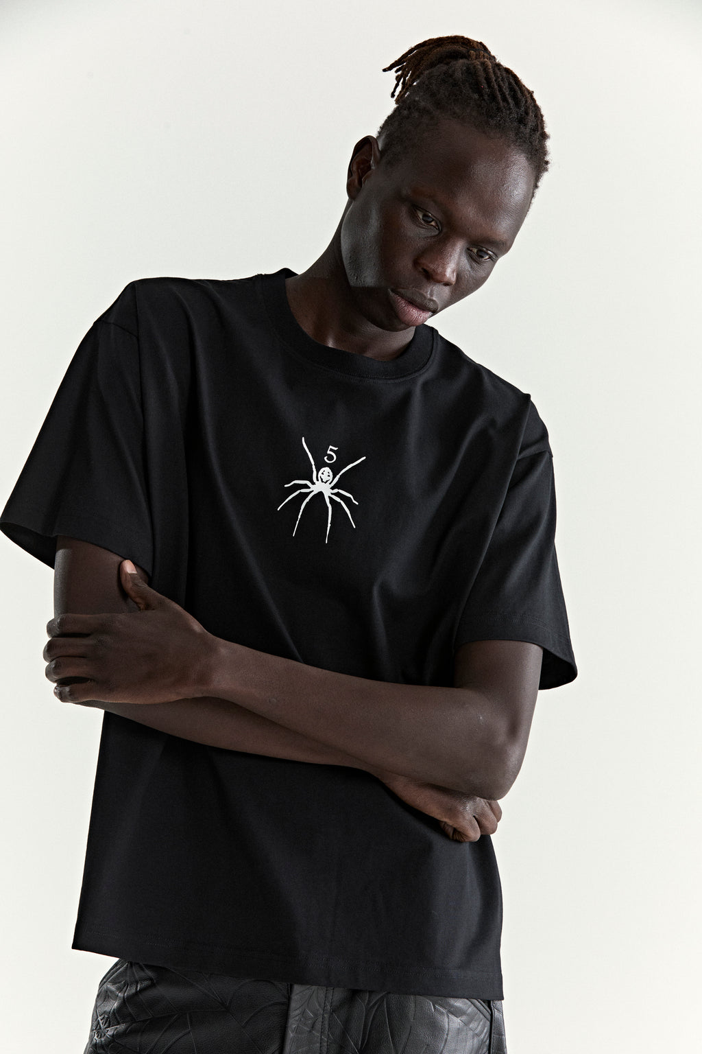 Black 100% cotton TM TEE with white spider graphic print on front, worn by a model.