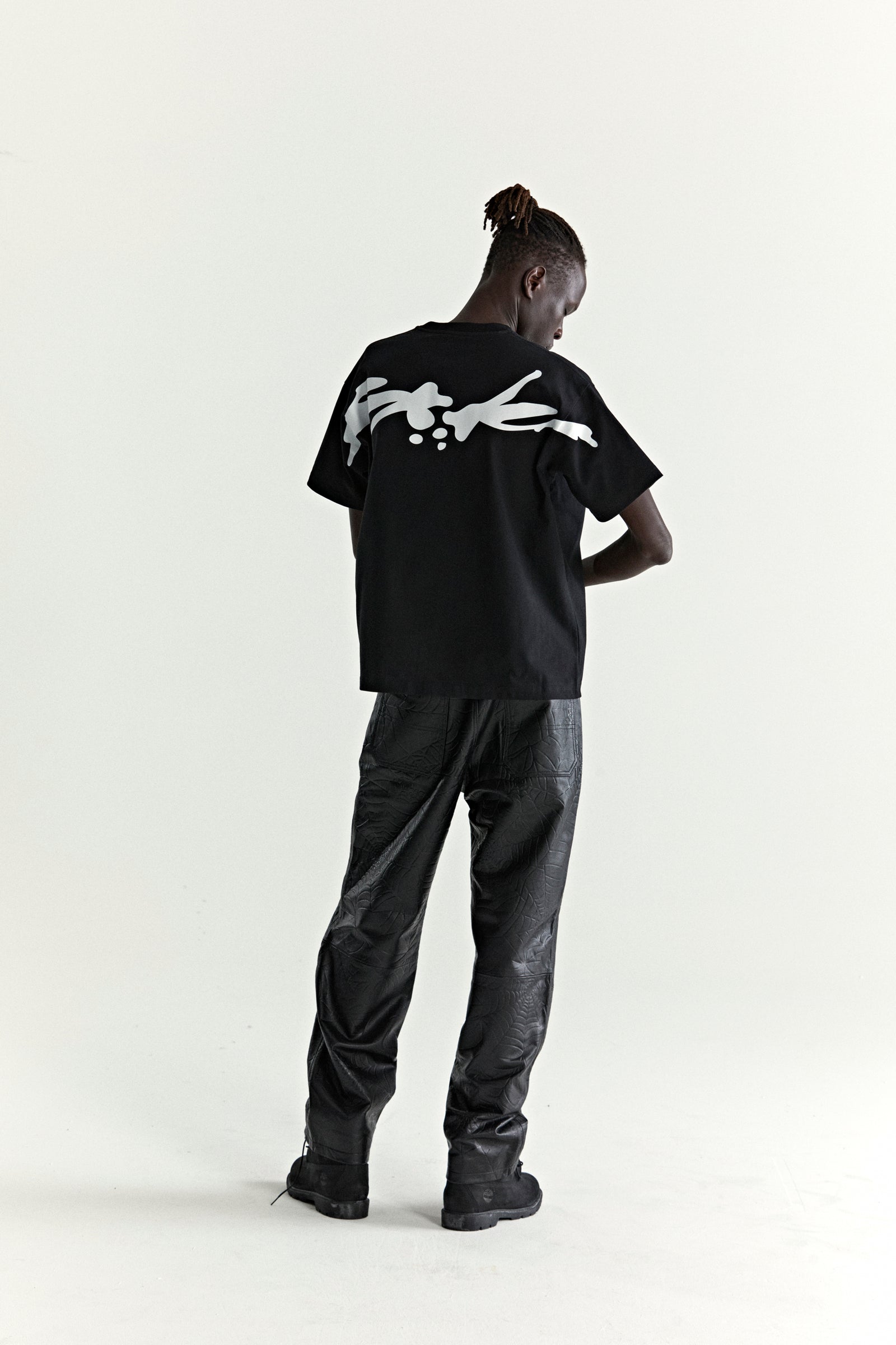 Black 100% cotton TM TEE with white graphic print on back, worn by a model.