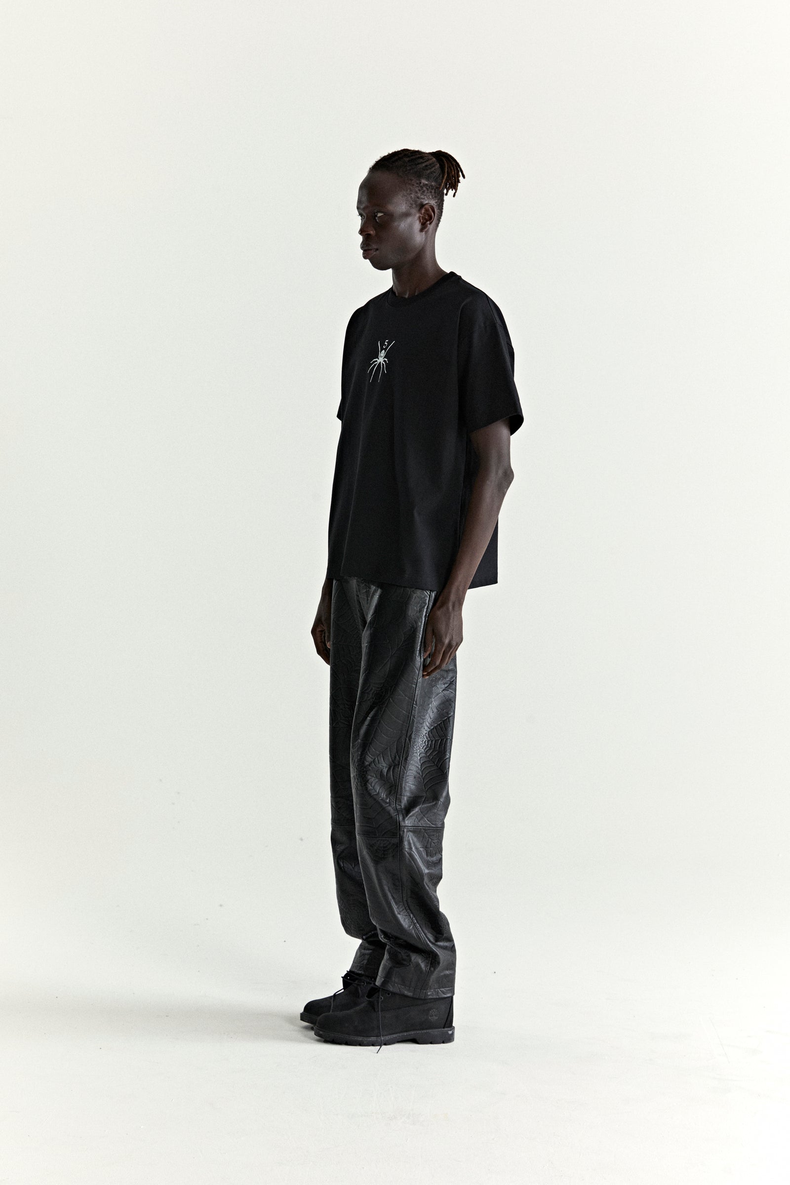 Black cotton TM TEE with white spider graphic, worn by a model with black textured pants.