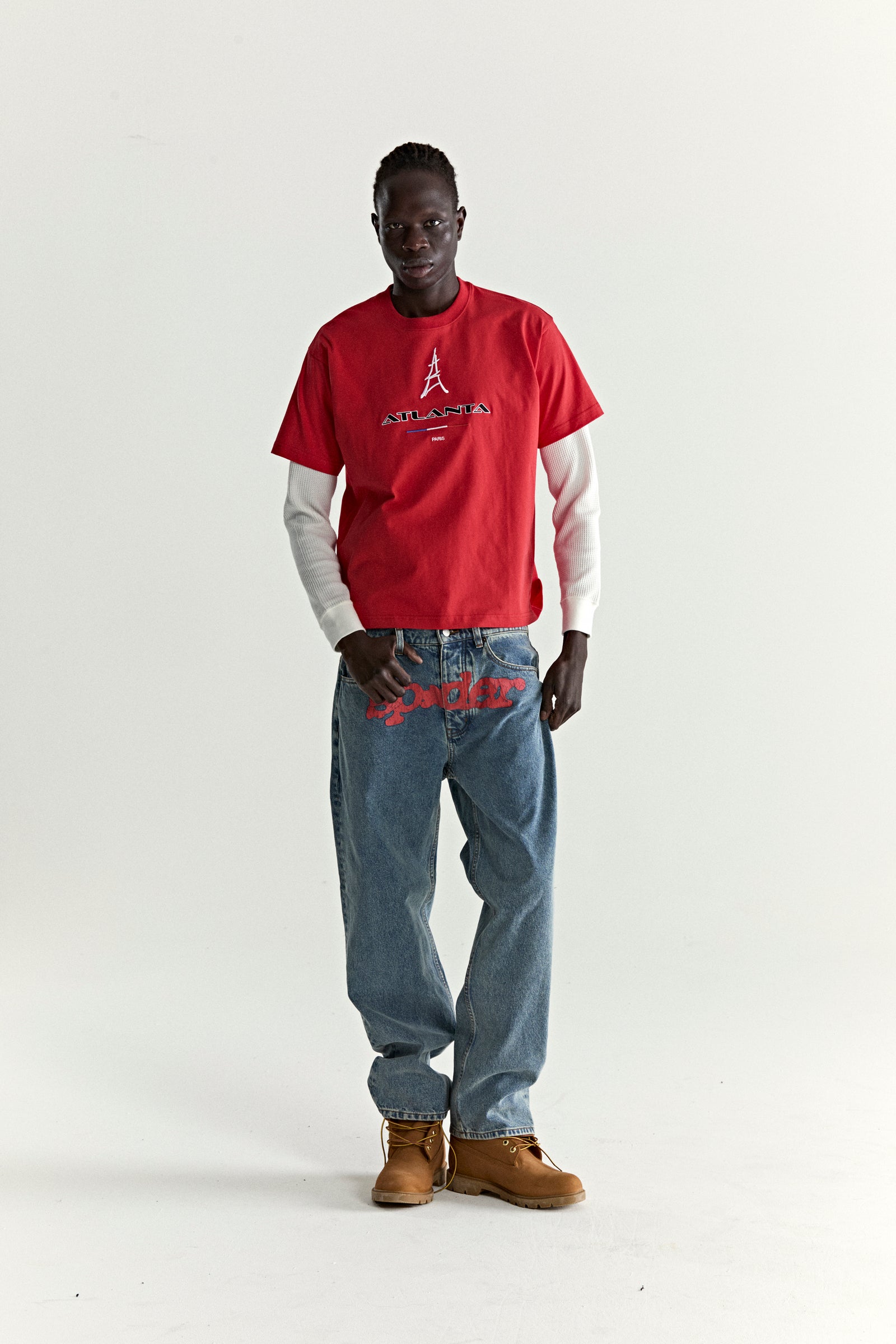 Red cotton ARAIGNÉE TEE with embroidered Eiffel Tower graphic, layered over a white long-sleeve, paired with blue jeans and brown boots.