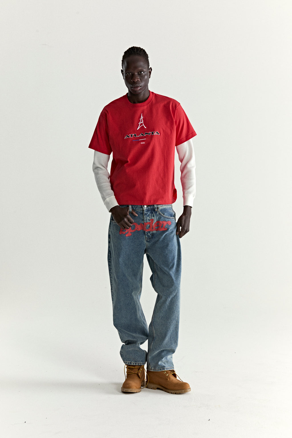 Red cotton ARAIGNÉE TEE with embroidered Eiffel Tower graphic, layered over a white long-sleeve, paired with blue jeans and brown boots.