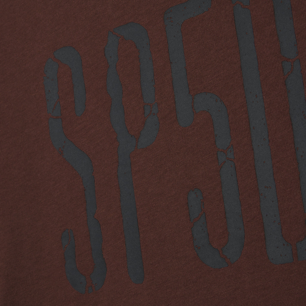 Brown 100% cotton tee featuring a dark grey graphic print with a distressed, cracked texture design.