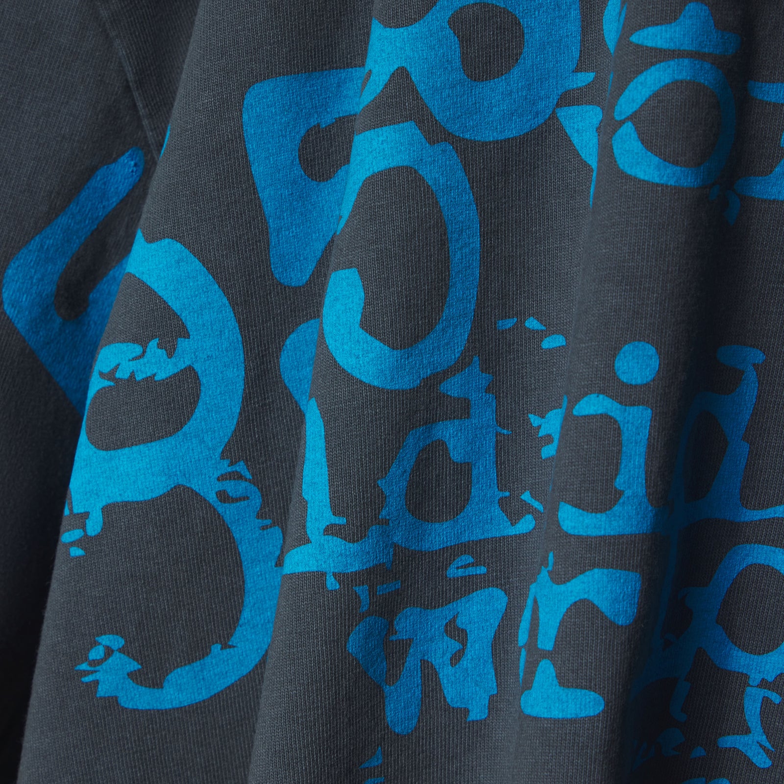 Close-up of a dark grey cotton tee with a distressed blue graphic print.