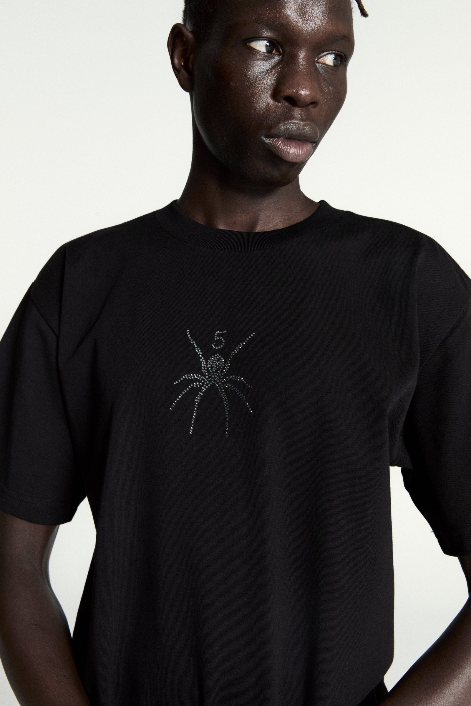 Black cotton tee with a rhinestone spider graphic and "5" on the front, worn by a model.