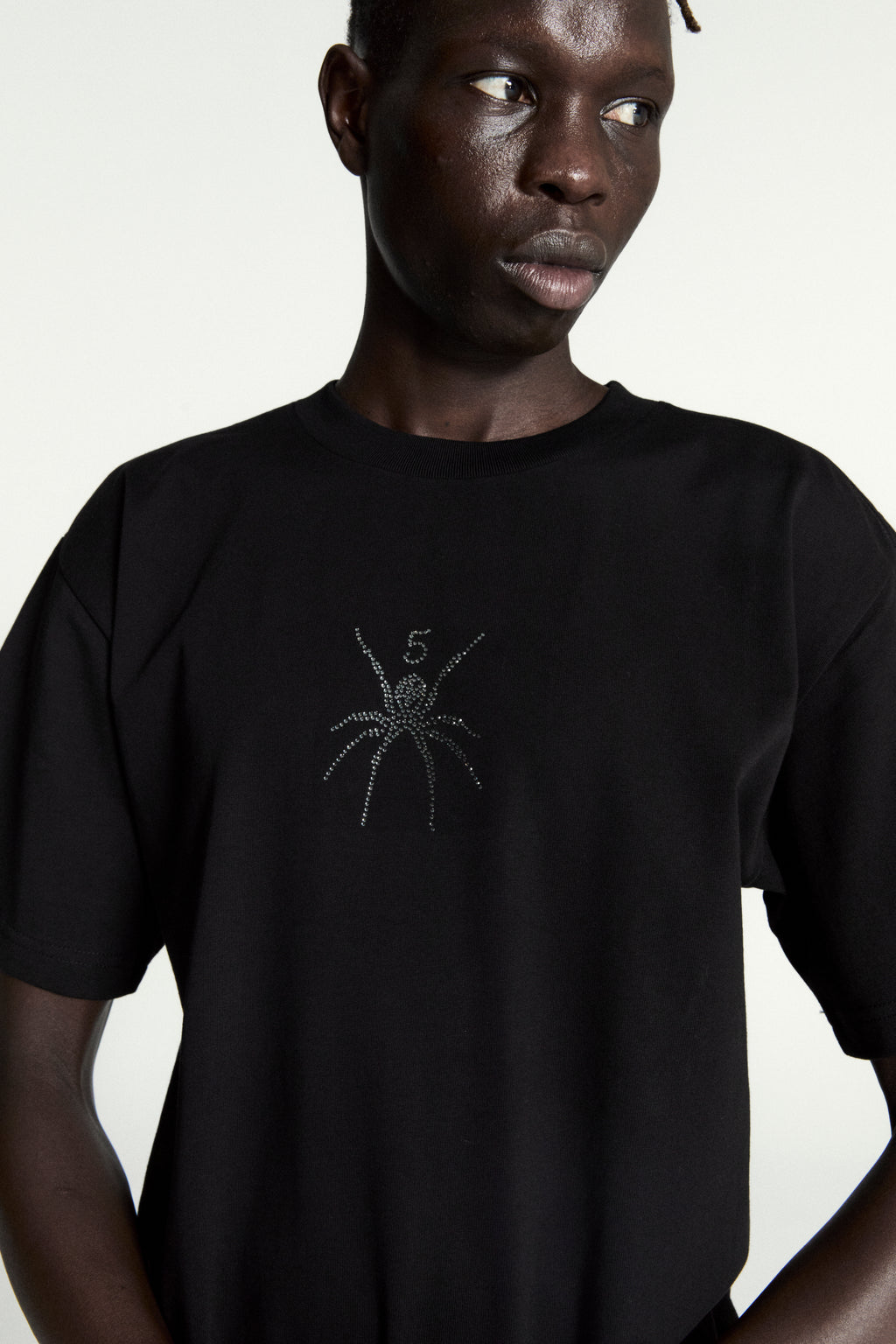 Black cotton tee with a rhinestone spider graphic and "5" on the front, worn by a model.