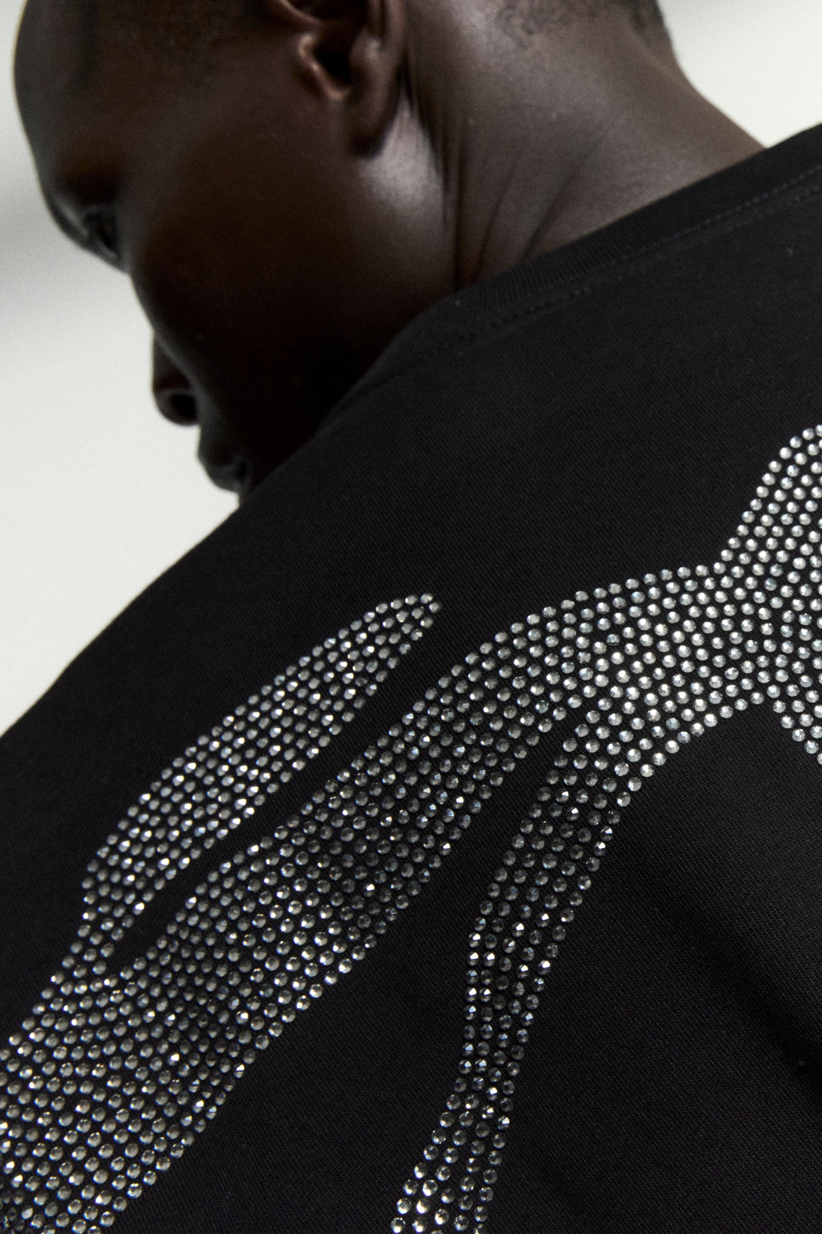Black 100% cotton tee with a sparkling rhinestone graphic on the back, worn by a person.