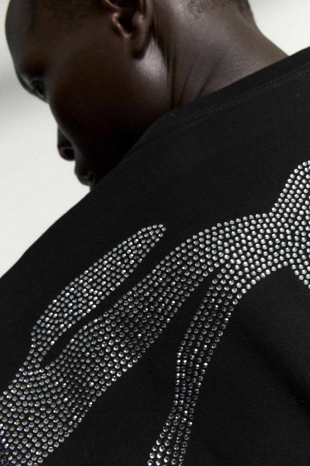 Black 100% cotton tee with a sparkling rhinestone graphic on the back, worn by a person.