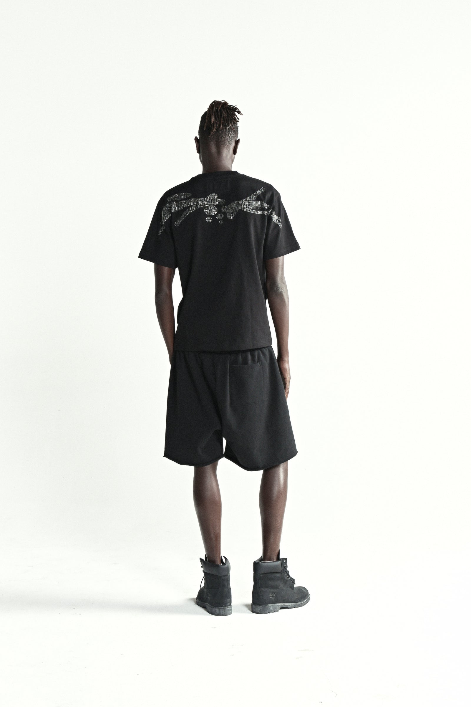 Man in black cotton rhinestone tee with back graphic and matching shorts.