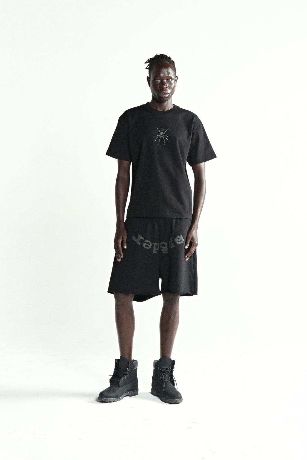 Black cotton tee with rhinestone spider graphic, worn by a man with black shorts and boots.