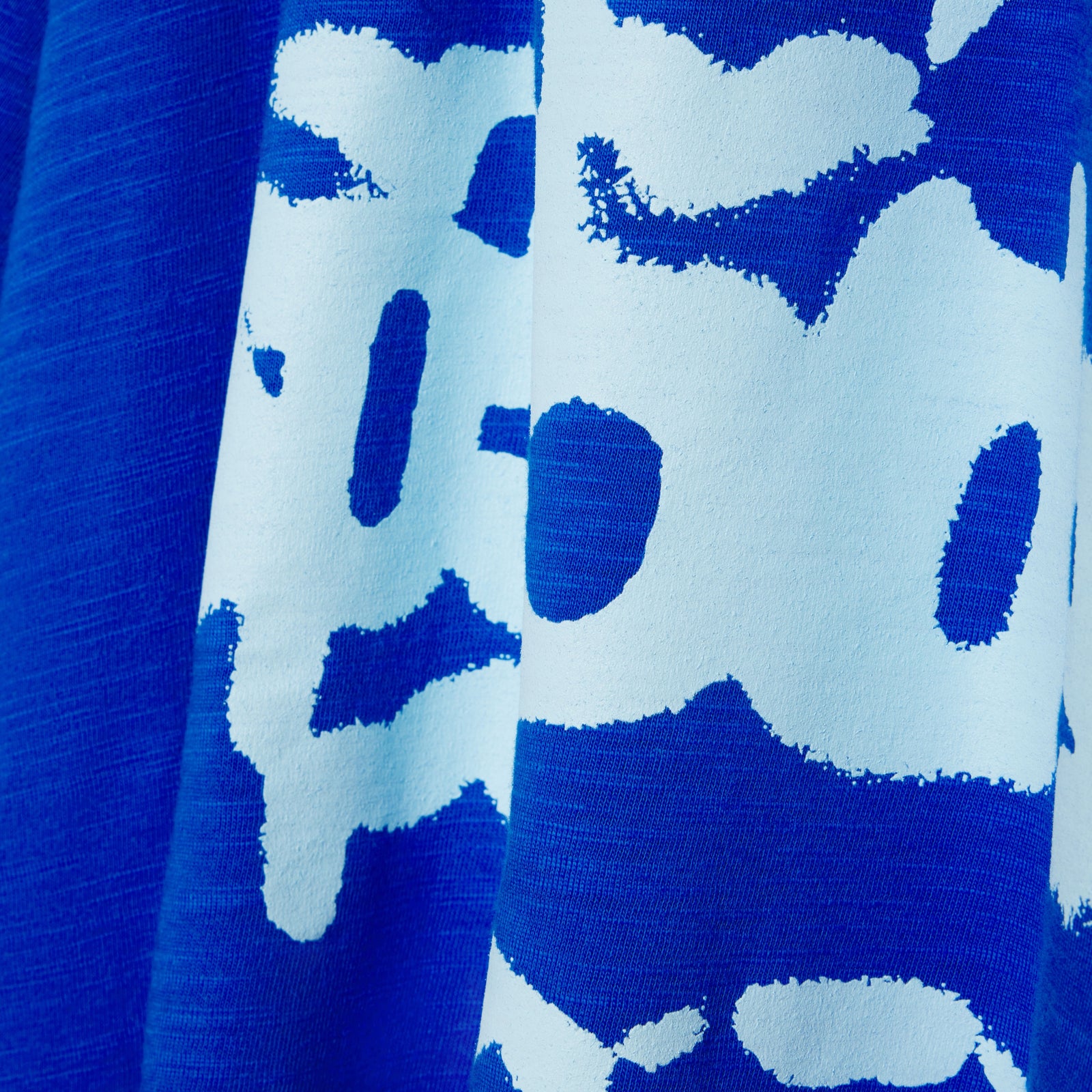 Close-up of blue slub jersey tee with white abstract graphic print and contrast stitching.