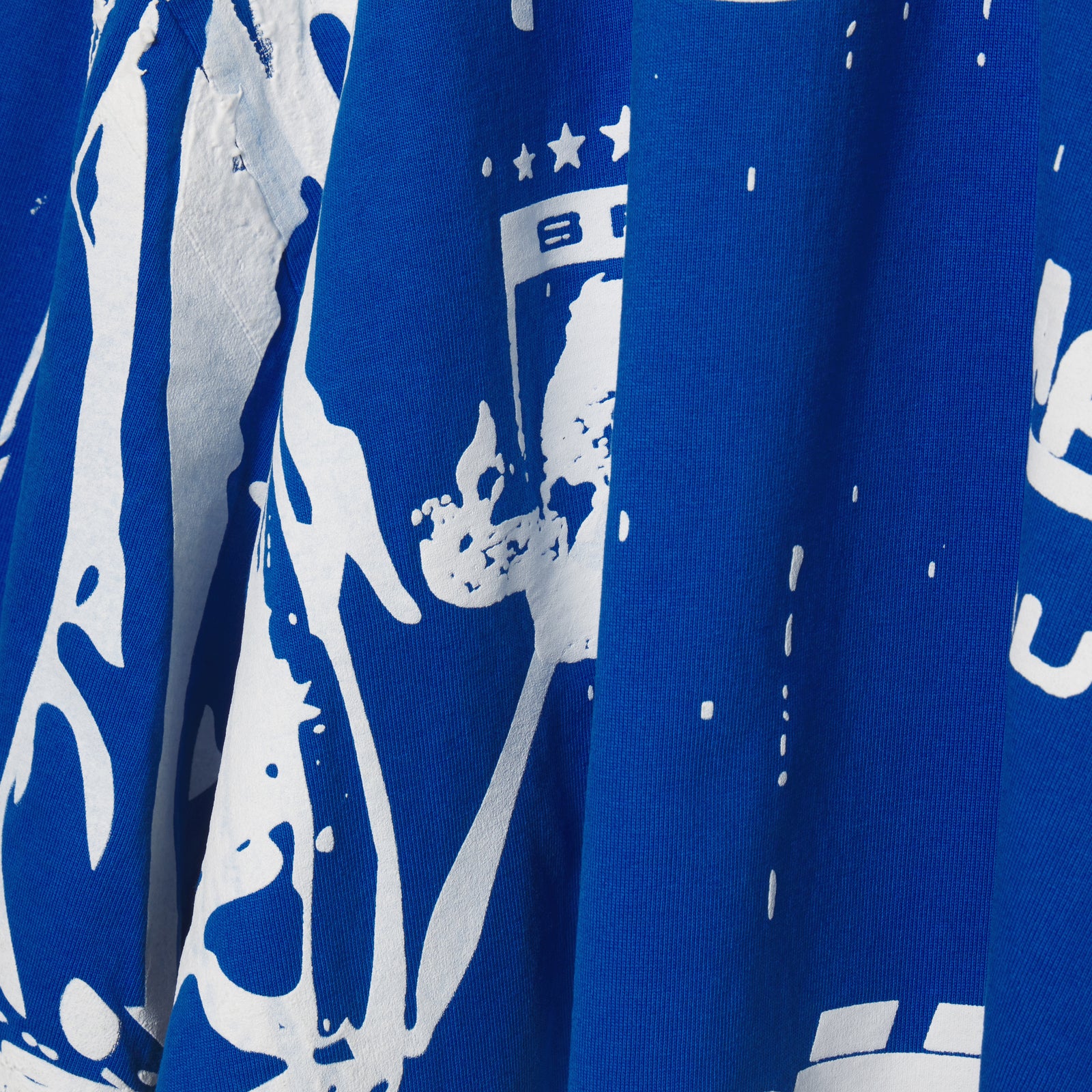 Close-up of a blue 100% cotton tee with a white trompe l'œil graphic print.