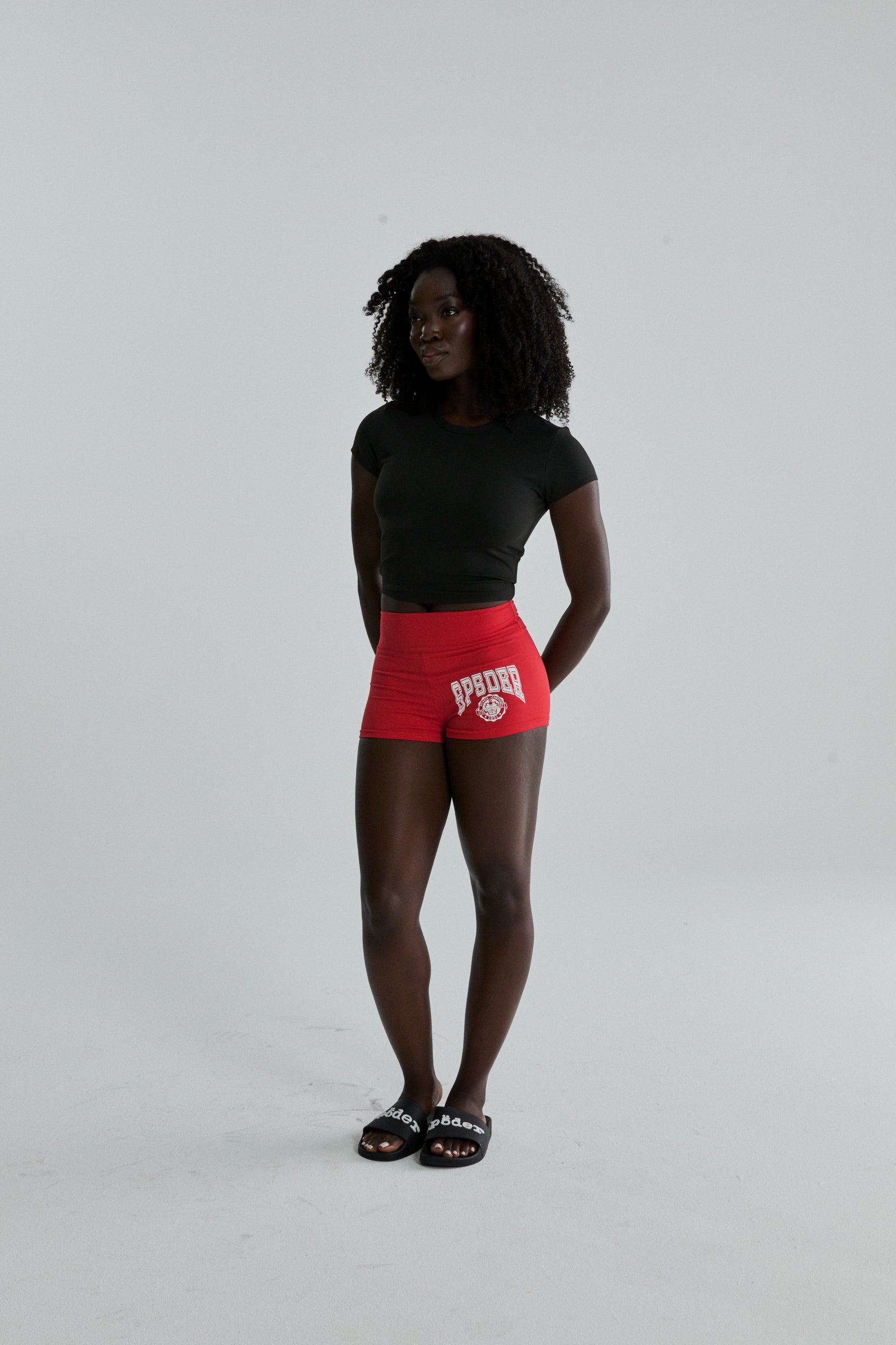Woman wearing red stretch cotton jersey SP5DER Tiny Short with collegiate graphic and black t-shirt.