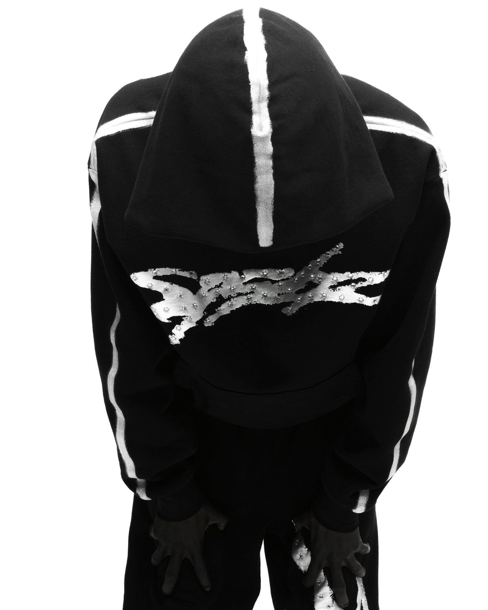 Black fleece hoodie with metallic "SP5DER" logo, rhinestone accents, and sprayed white stripes.