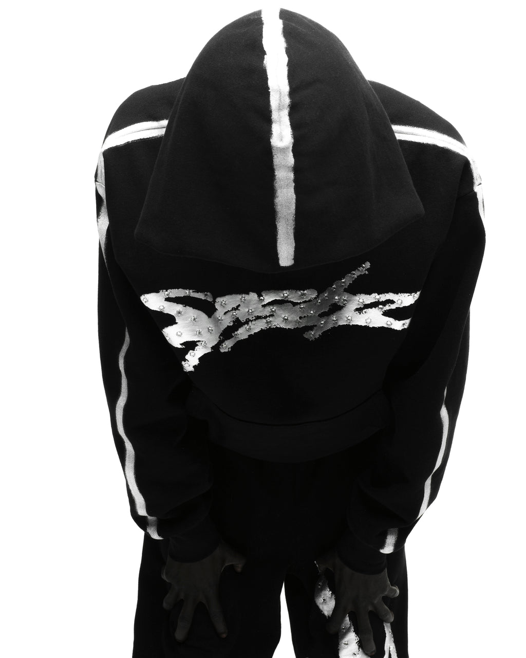 Black fleece hoodie with metallic "SP5DER" logo, rhinestone accents, and sprayed white stripes.