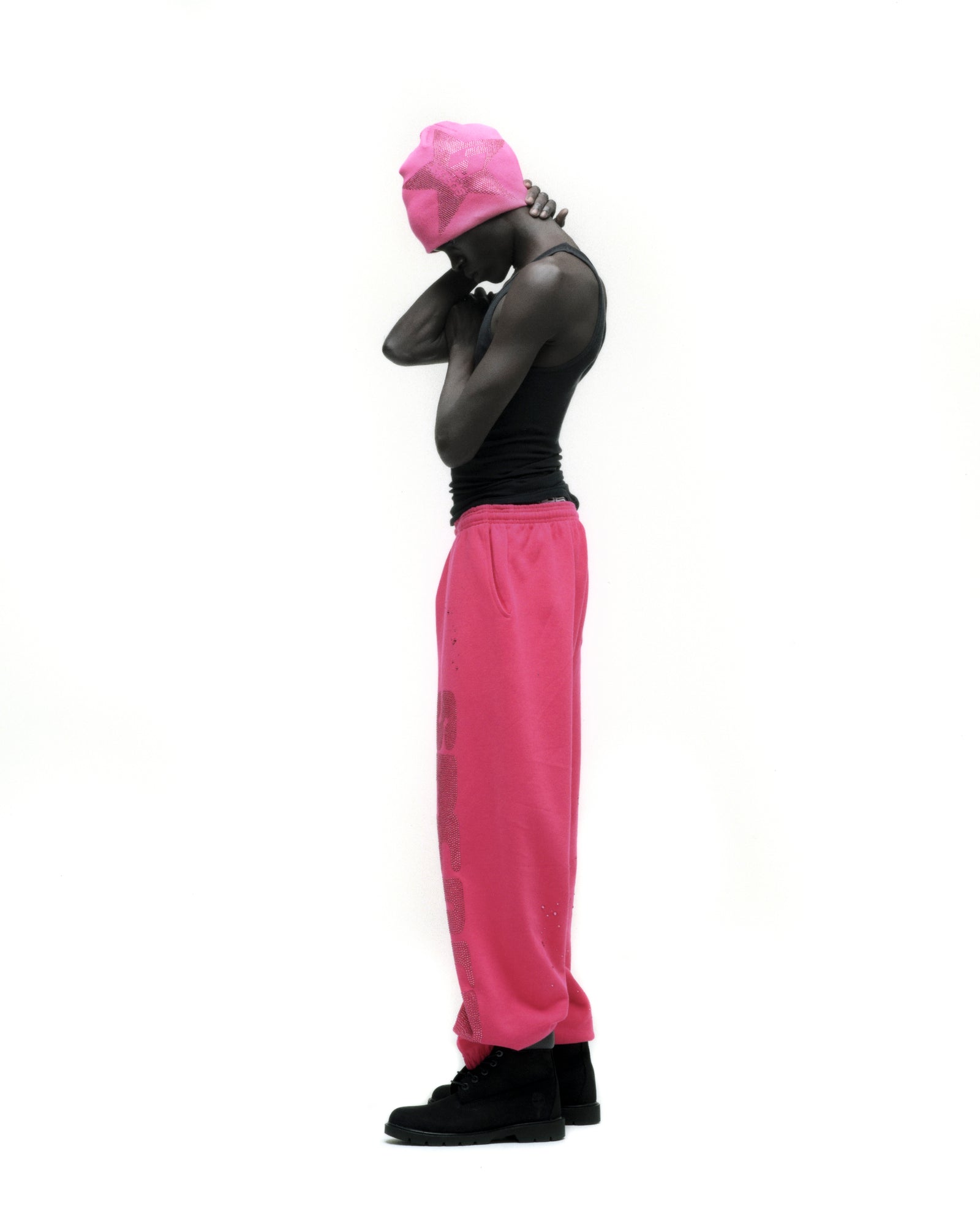 Man in hot pink rhinestone silk sweatpants, black tank top, and matching pink beanie.