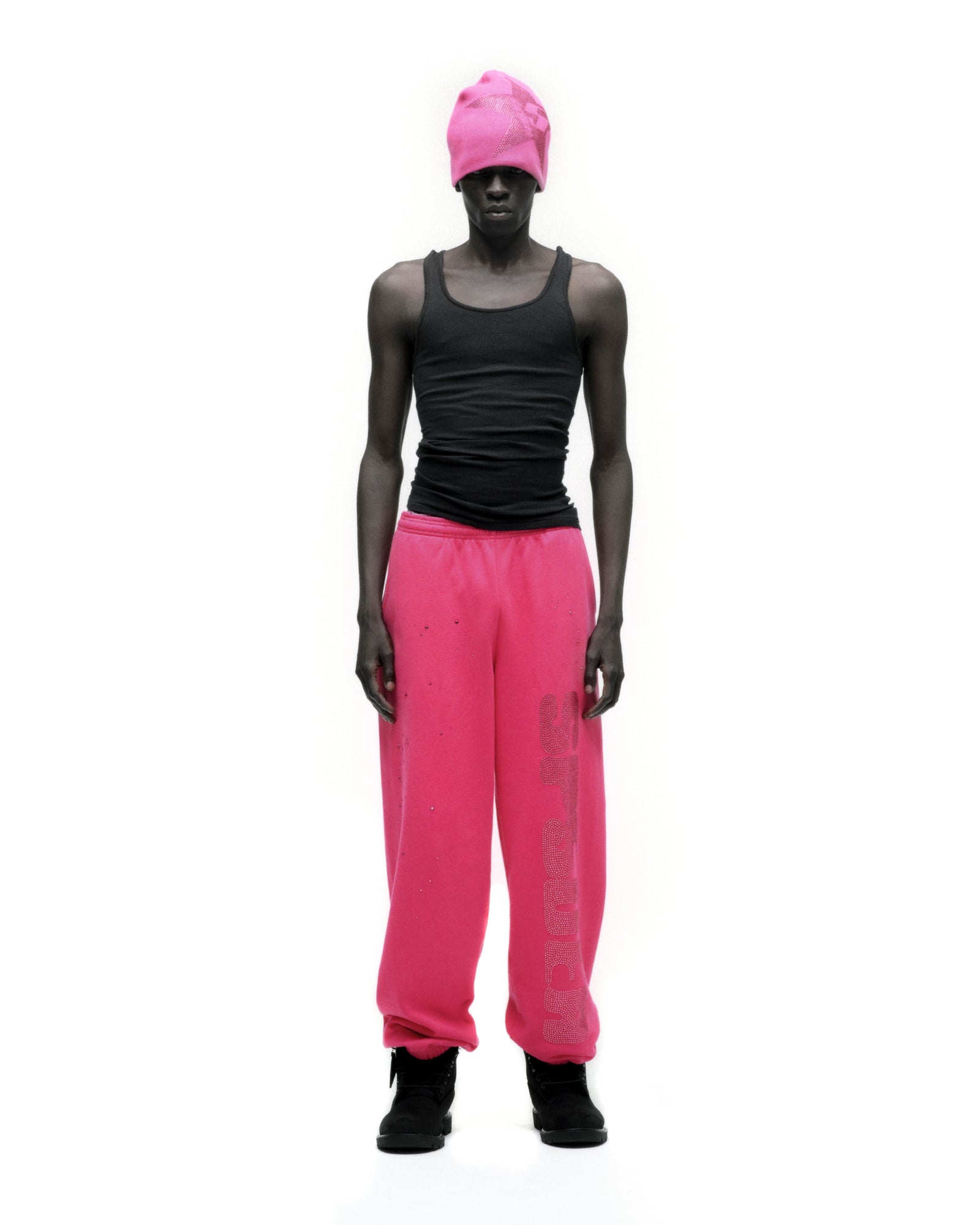 Man in hot pink rhinestone silk sweatpants with black tank top and beanie.