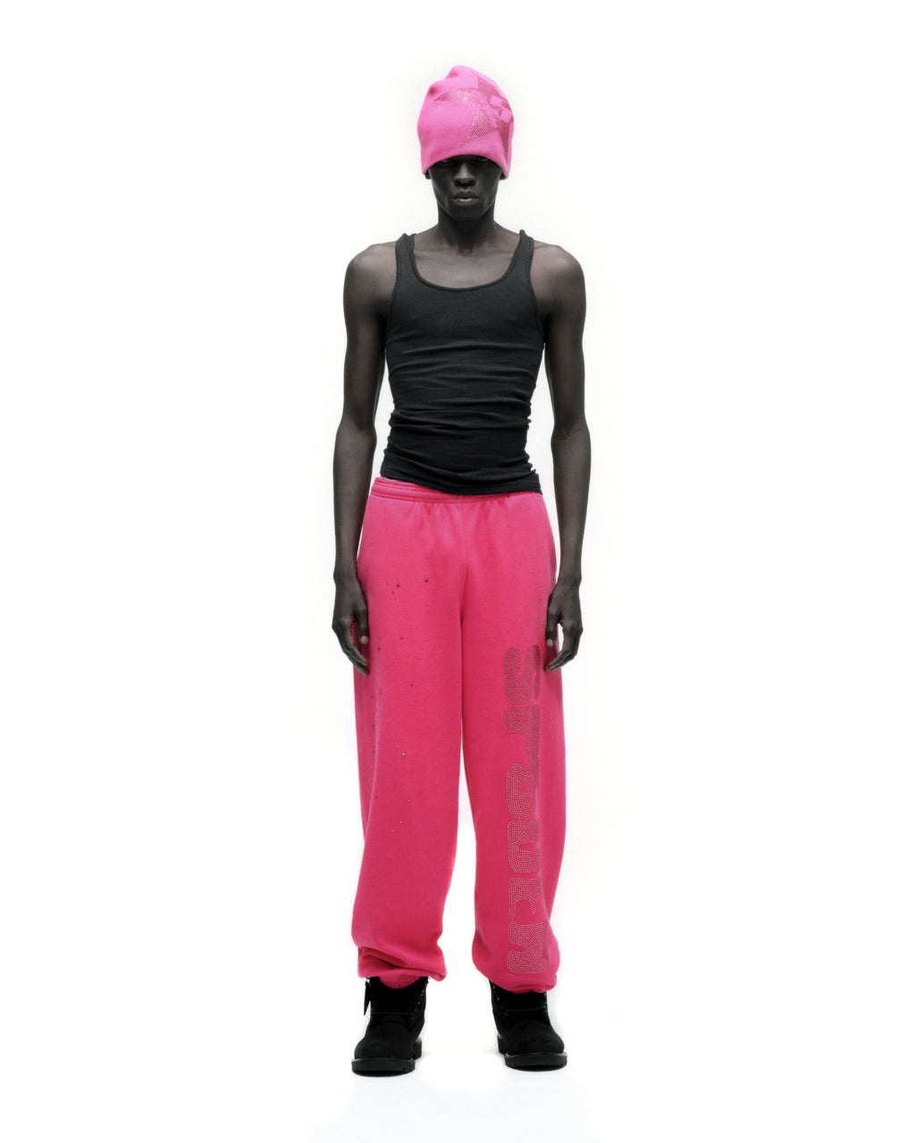 Man in hot pink rhinestone silk sweatpants with black tank top and beanie.
