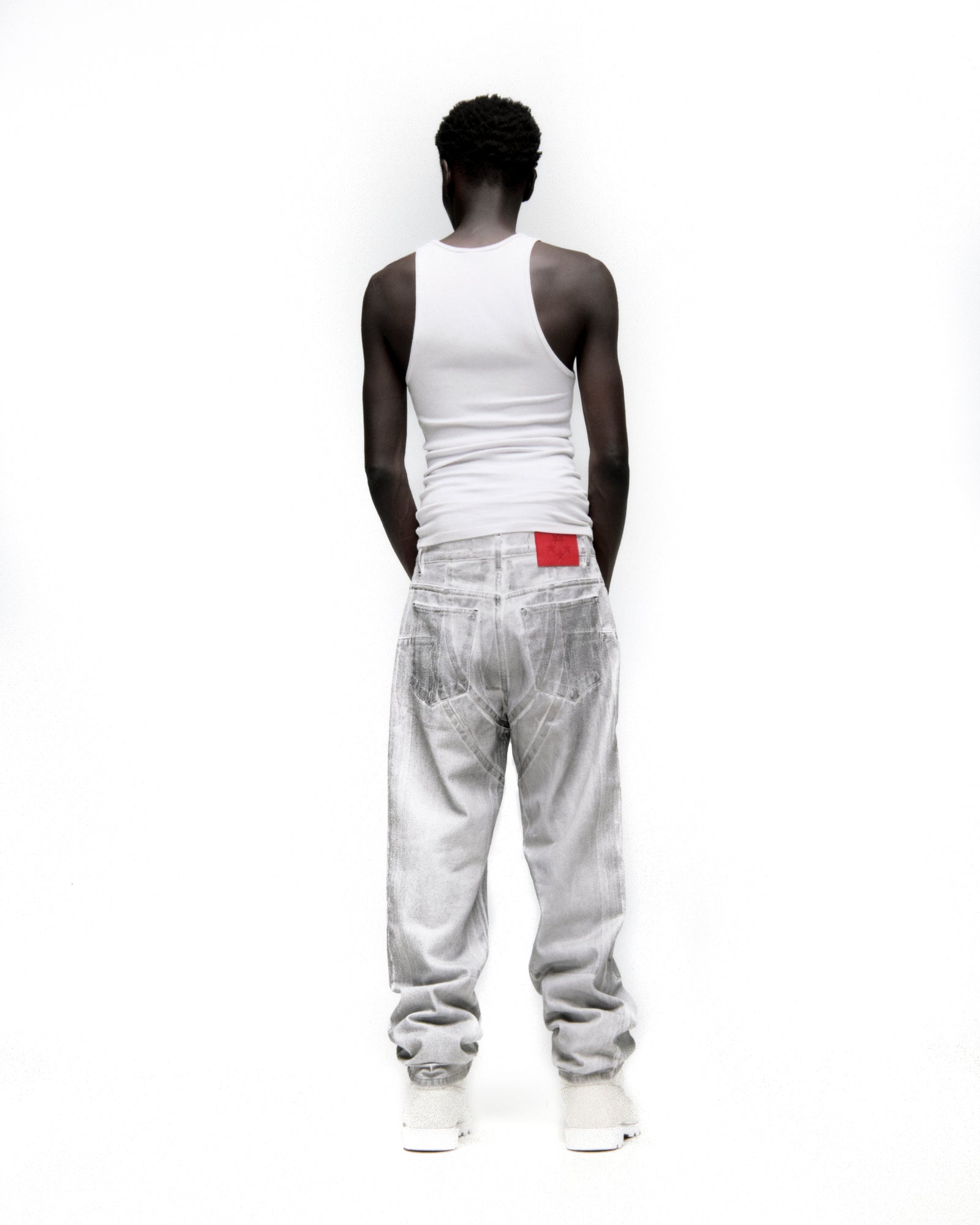 Man from behind wearing platinum spray-effect wide-leg denim pants with a red branded back patch.