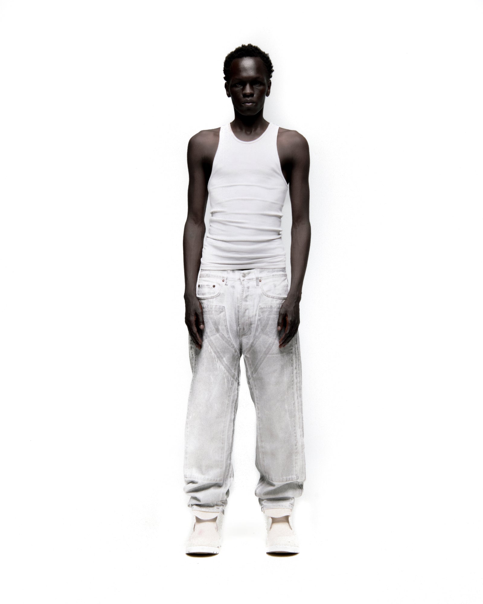 Man in Platinum Denim Pant, wide leg, spray-effect light wash, with front panels and white tank top.