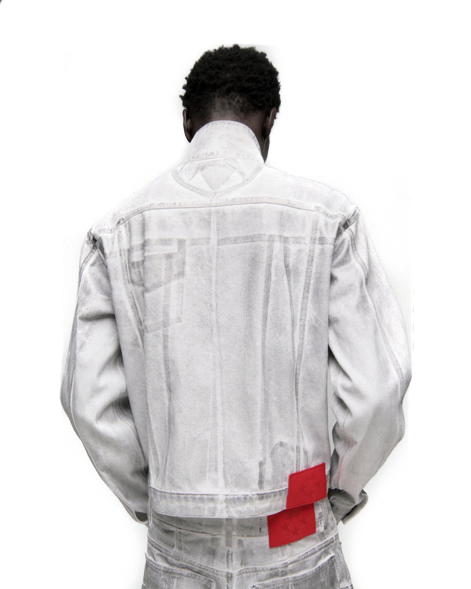 Back of a man wearing a platinum spray-effect denim trucker jacket with red leather patches.